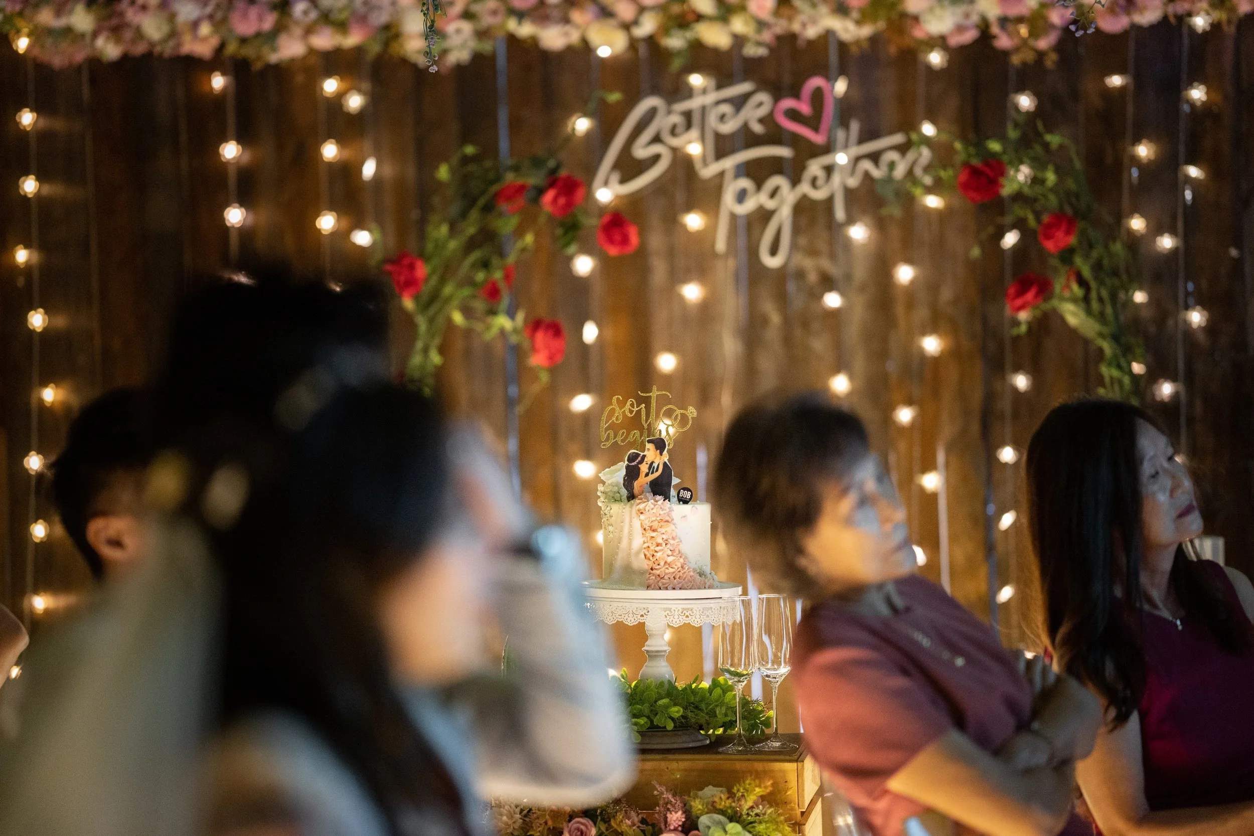 People sitting at a decorated wedding reception with a cake on the table and a bridal shower sign in the background.