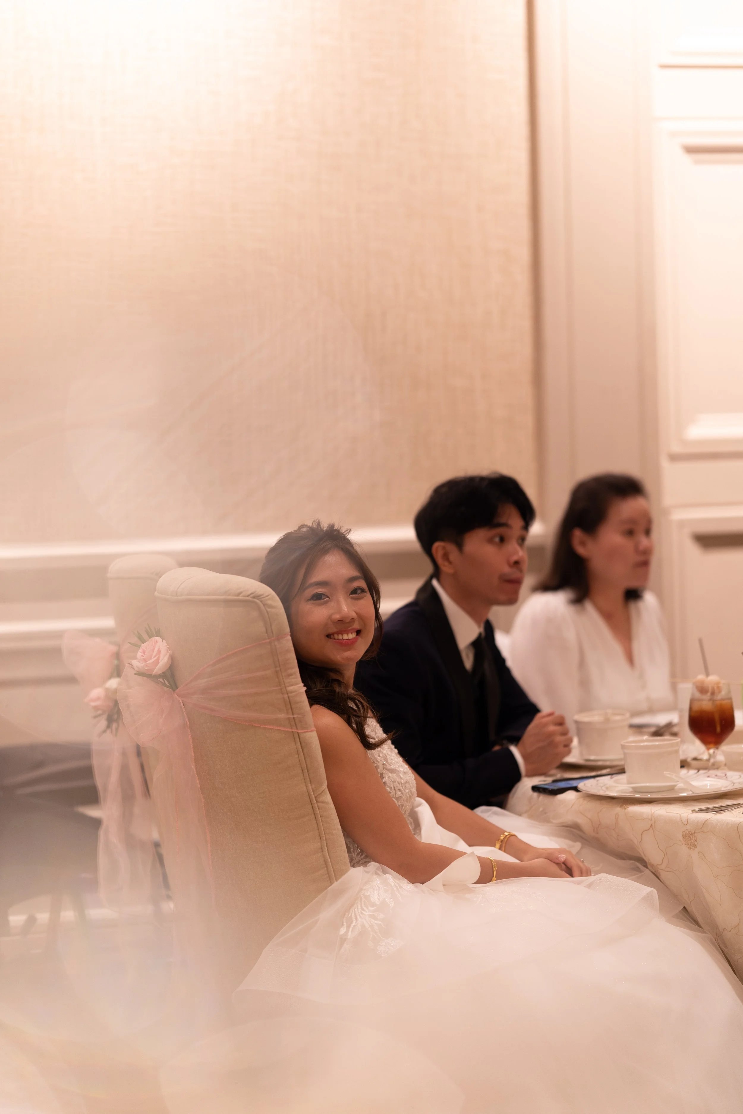 A smiling bride in a white wedding dress sitting at a banquet table with friends or family.
