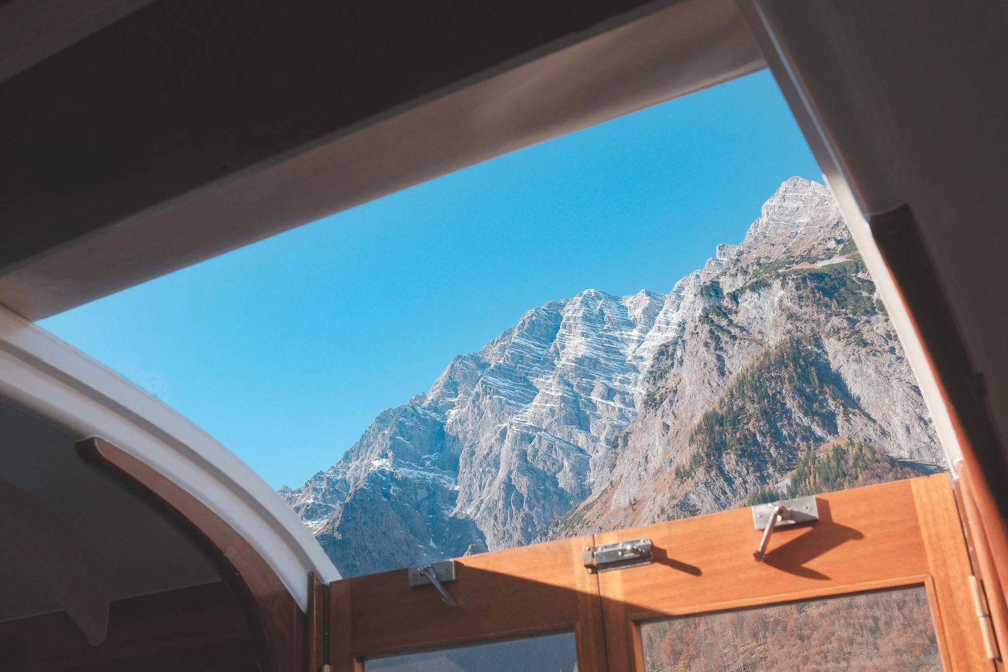 View of snow-capped mountain and blue sky seen through open window of a vehicle