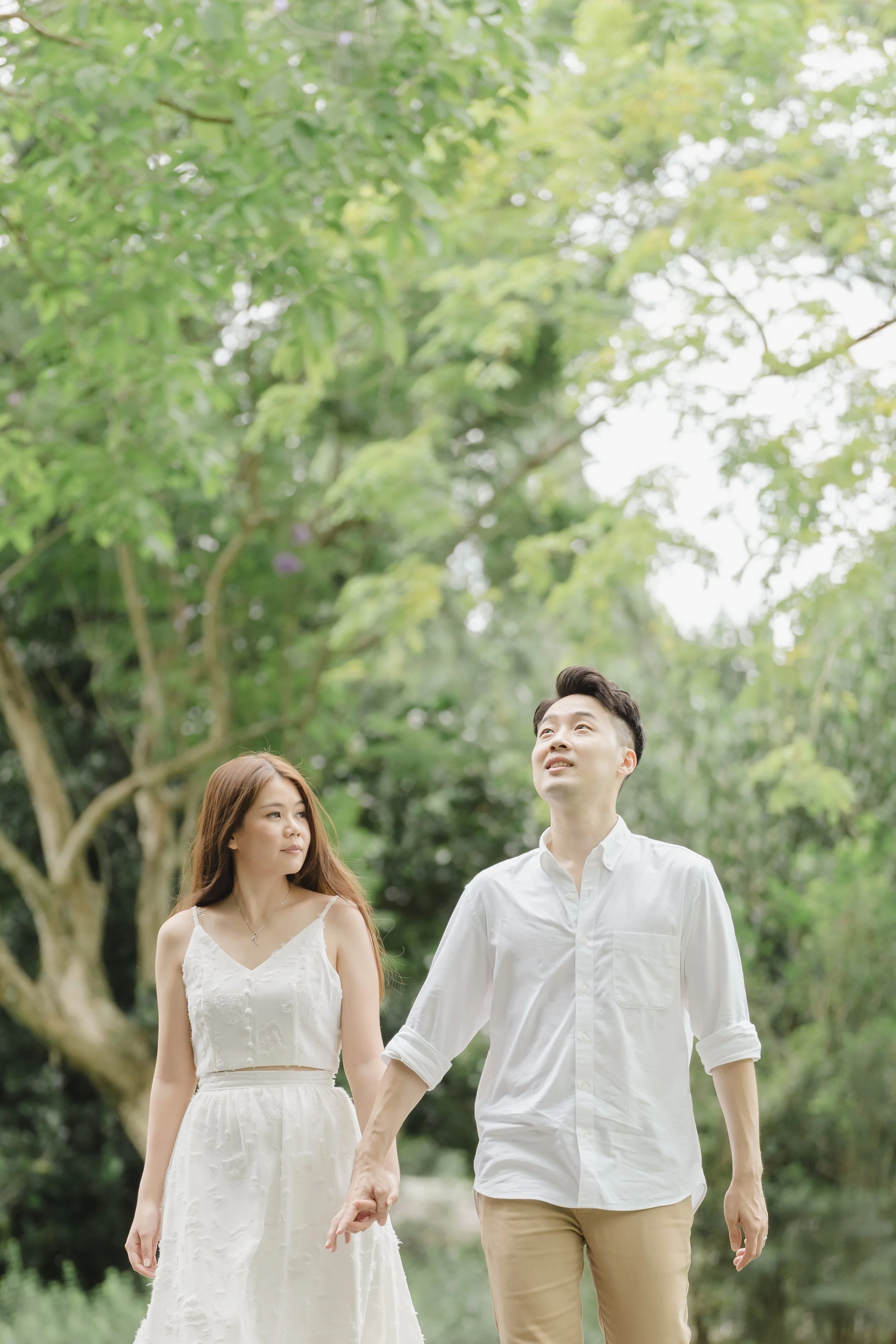 A young couple holding hands and walking through a lush green park with trees, enjoying a sunny day.
