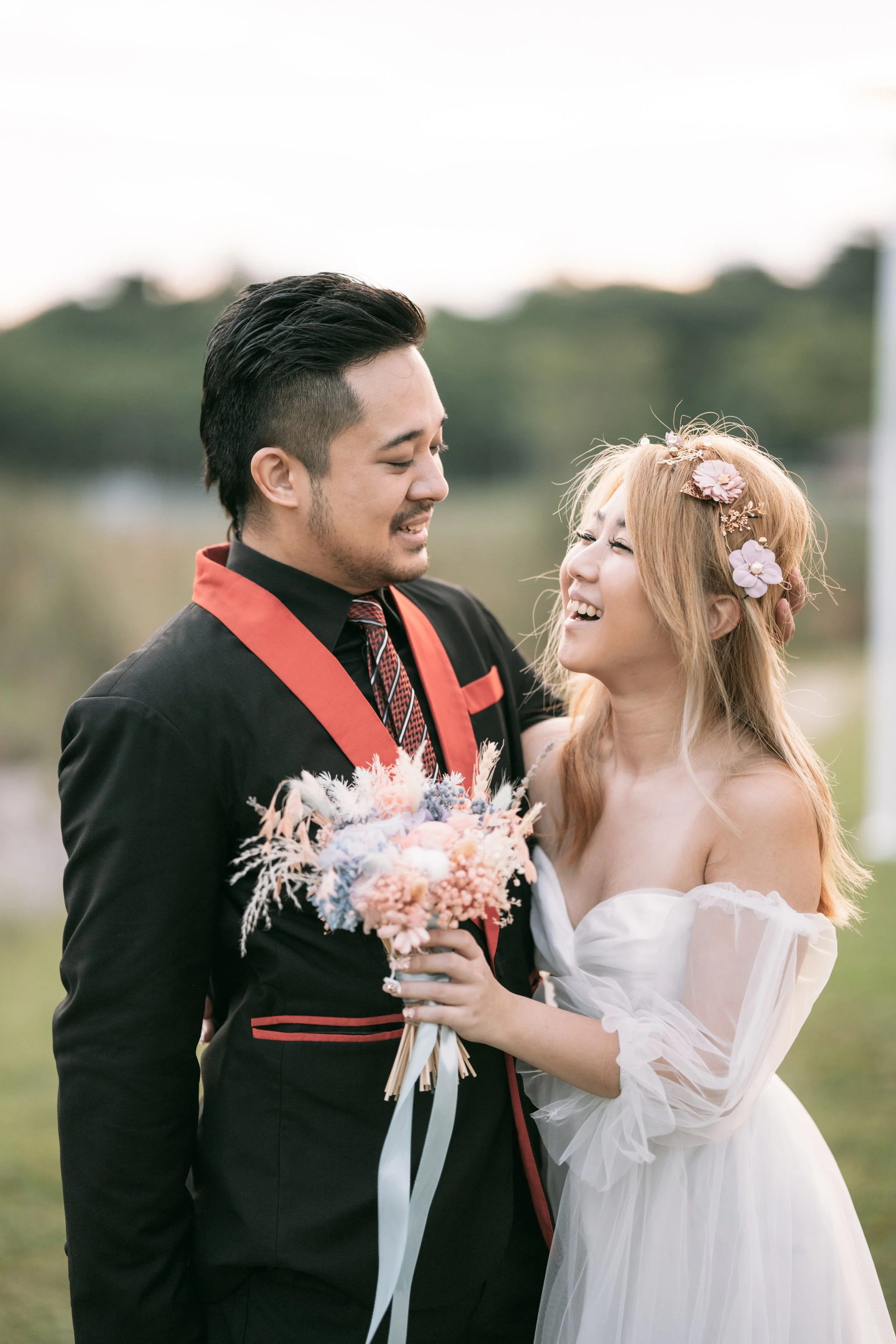 A couple in wedding attire enjoying a moment outdoors, with the woman holding a bouquet of flowers and wearing floral hair accessories.