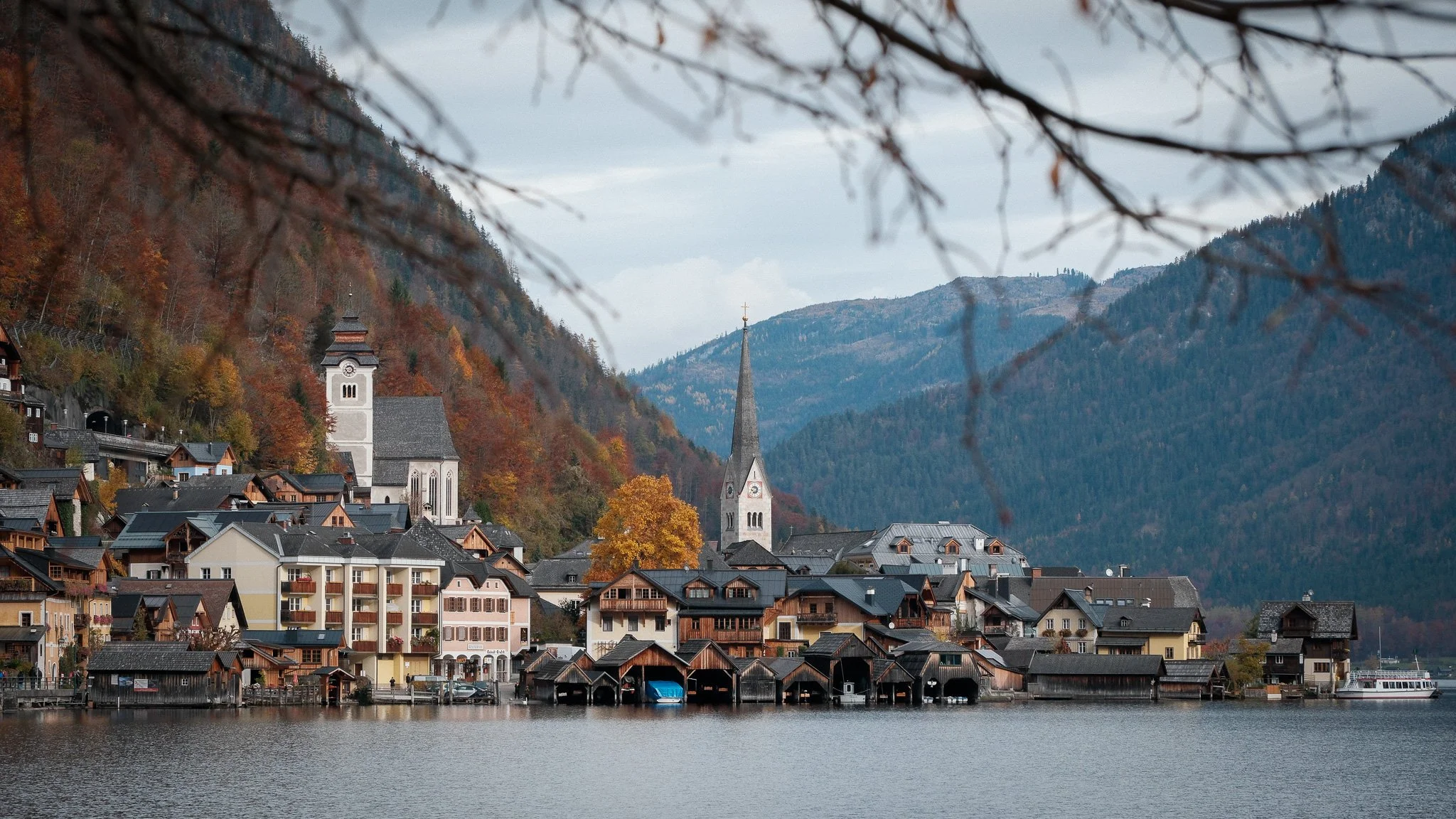 Scenic view of a lakeside village with colorful houses, church steeples, surrounded by mountains and autumn foliage.