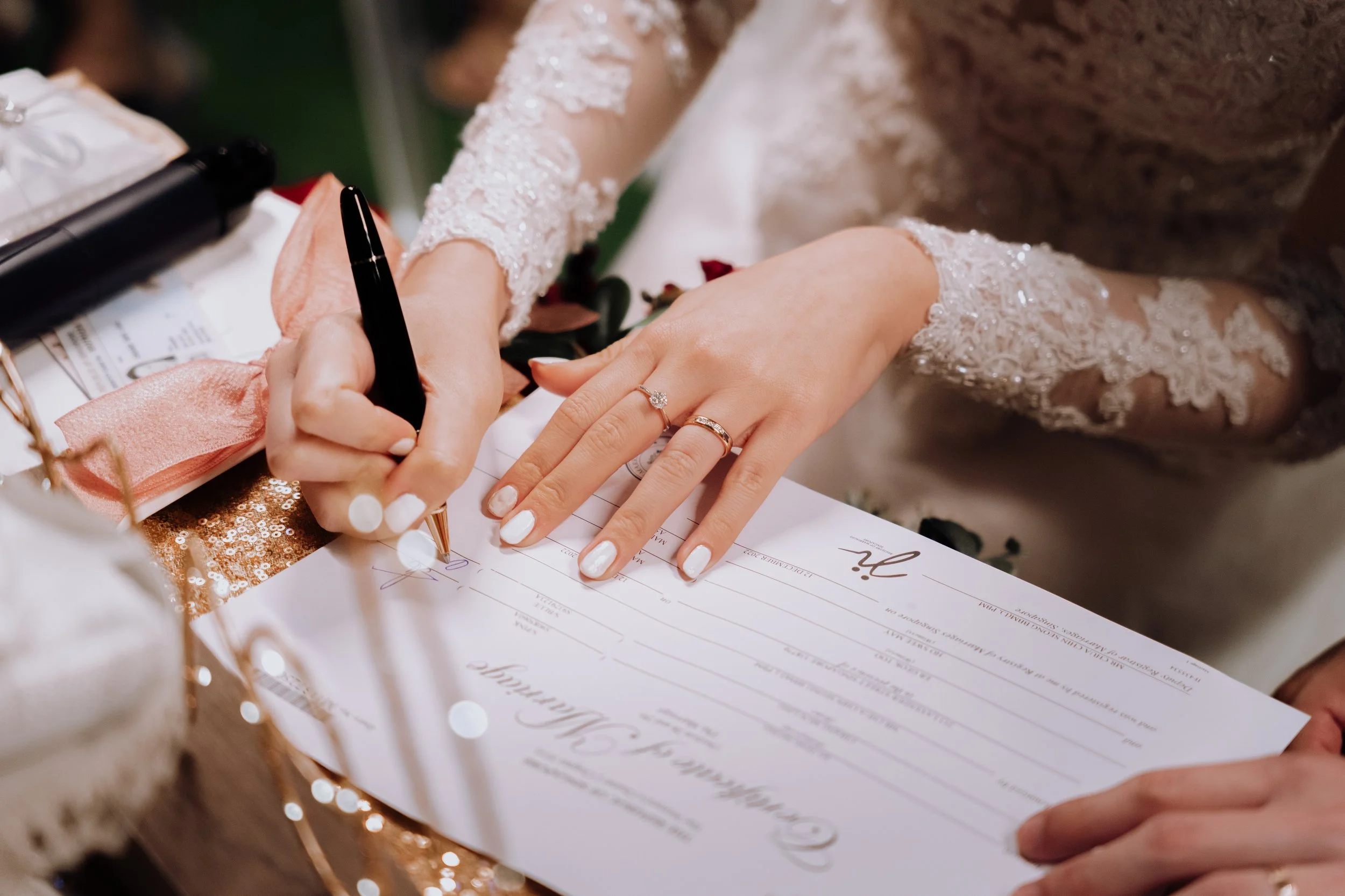 A bride signing a marriage certificate during her wedding ceremony, with her left hand displaying wedding rings.