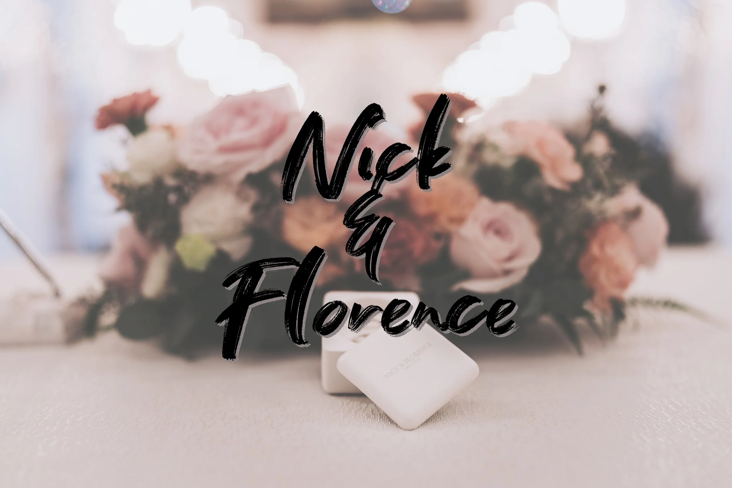 A floral arrangement of pink and white flowers on a table, with a blurred background. The text "Nick & Florence" is overlaid in black, stylish handwritten font.