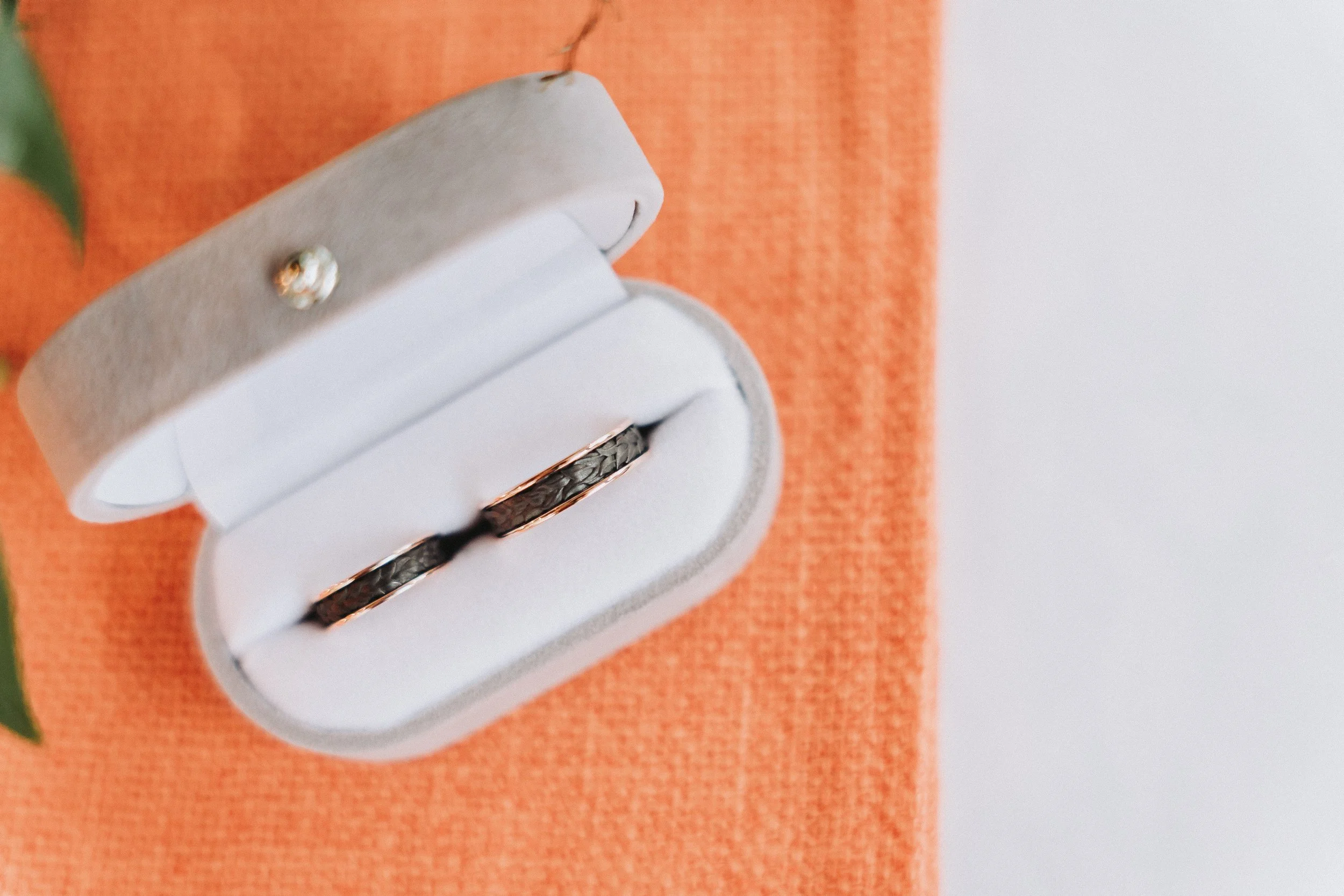 Two rings in a white ring box placed on an orange cloth surface.