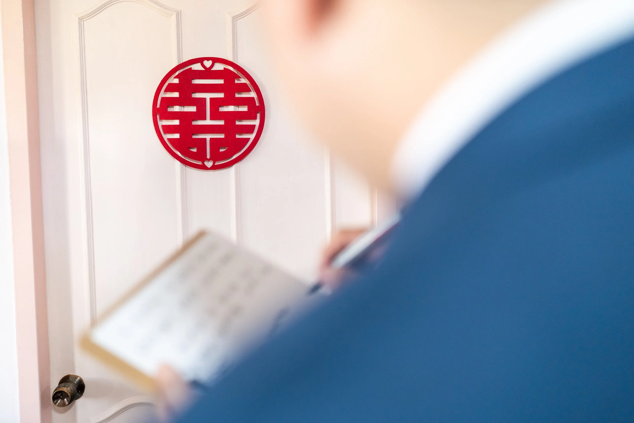 A person holding an open book, with a white door and a red circular Chinese paper cut decoration on the wall in the background.