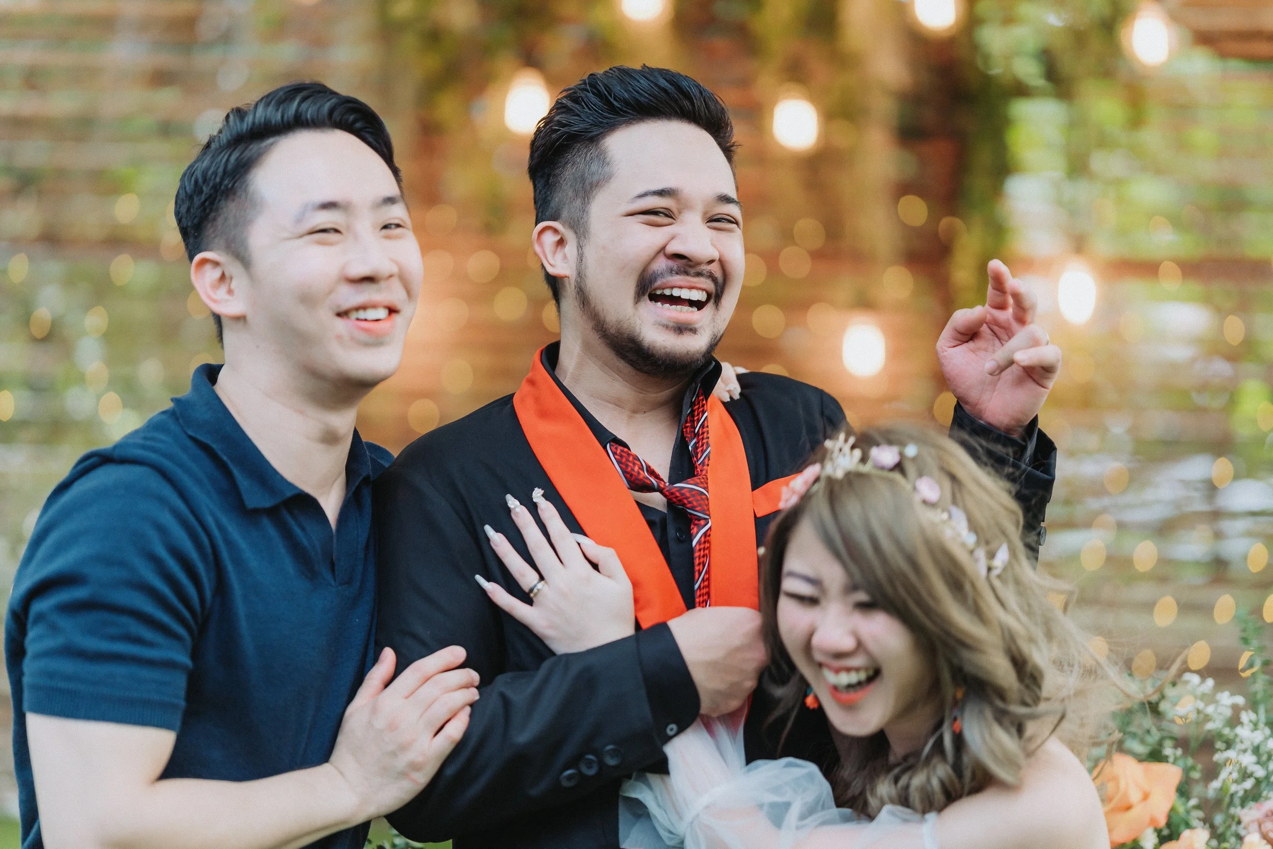Group of three friends laughing and enjoying a celebration outdoors, with bokeh lights in the background.