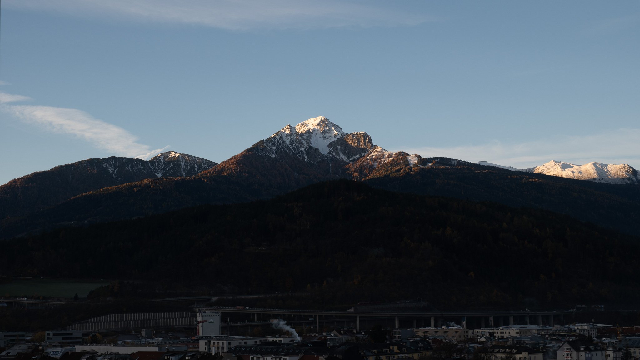 Mountain landscape with snow-capped peaks in the distance and a town in the foreground.