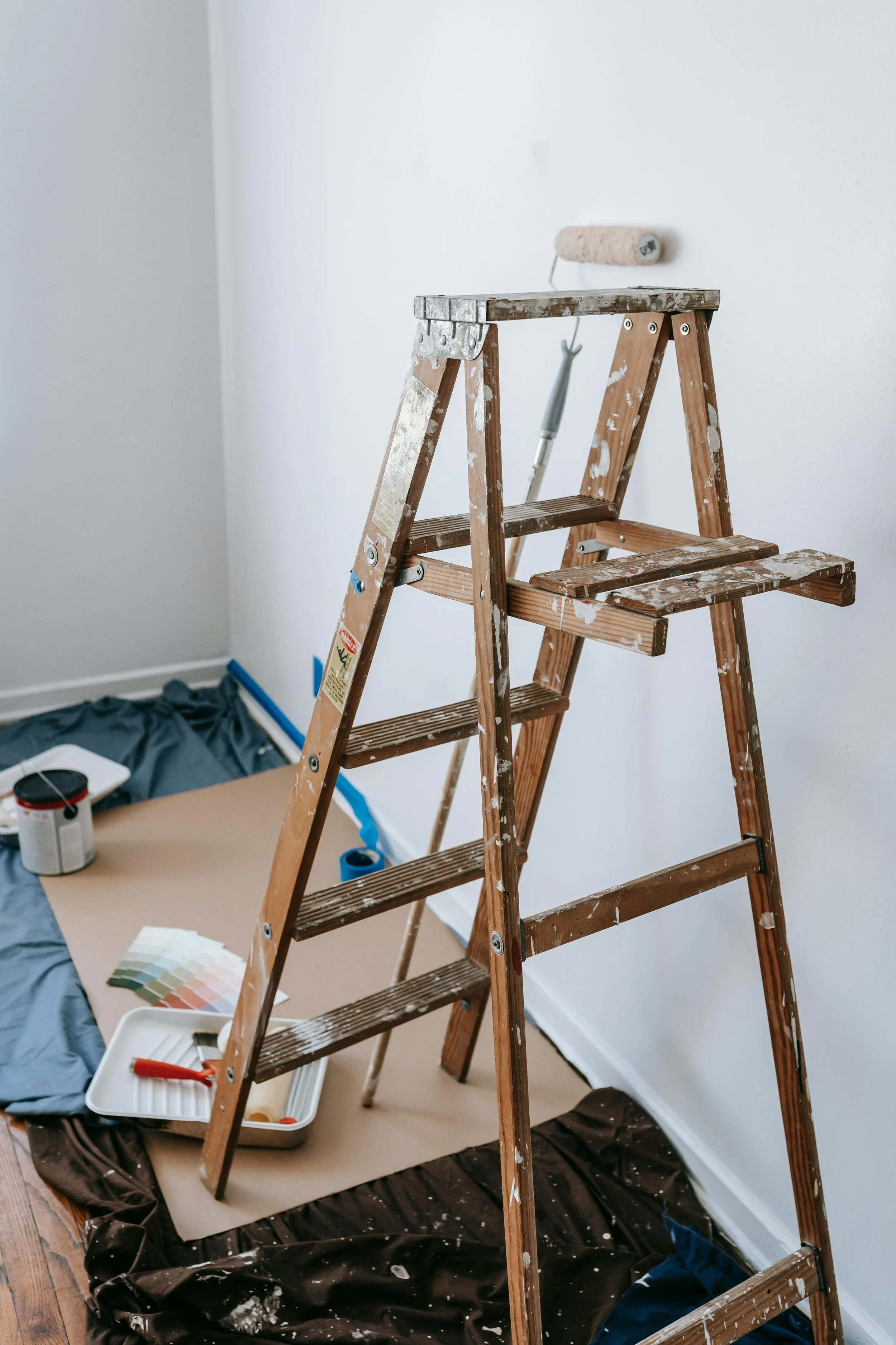Échelle en bois dans une pièce en cours de peinture, avec des outils et des échantillons de peinture au sol, bureau ou zone de travail