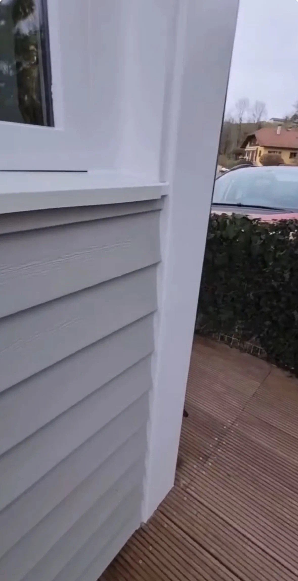 Close-up de l'extérieur d'une maison avec des murs en panneaux de revêtement en vinyle blanc, montrant la jonction entre le mur et le cadre de la fenêtre au coin.
