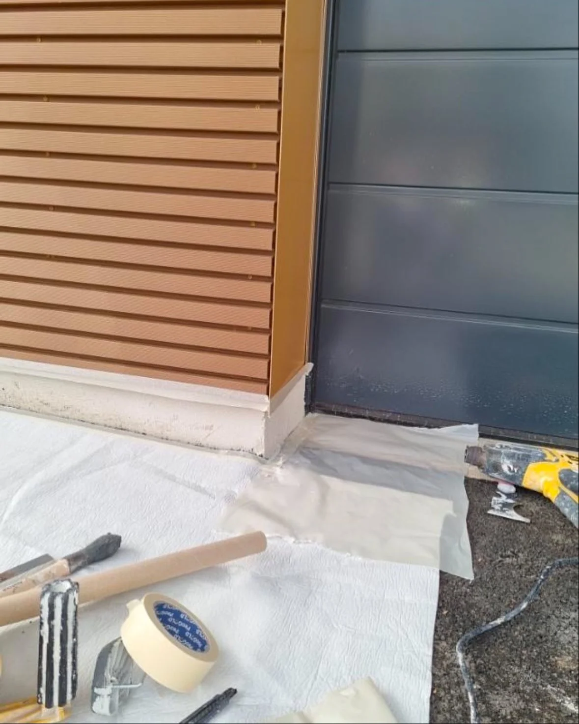 Travaux de finition autour d'une porte d'entrée avec un joint en cours d'application, outils et ruban adhésif sur le sol.