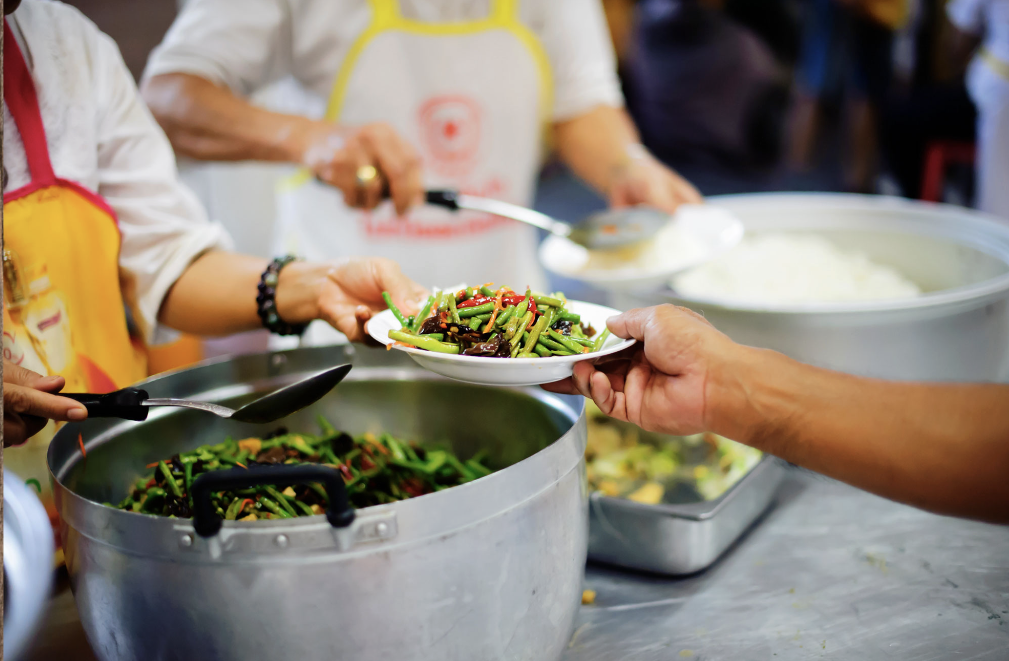 Person serving a plate of mixed vegetables at a buffet or food service station.