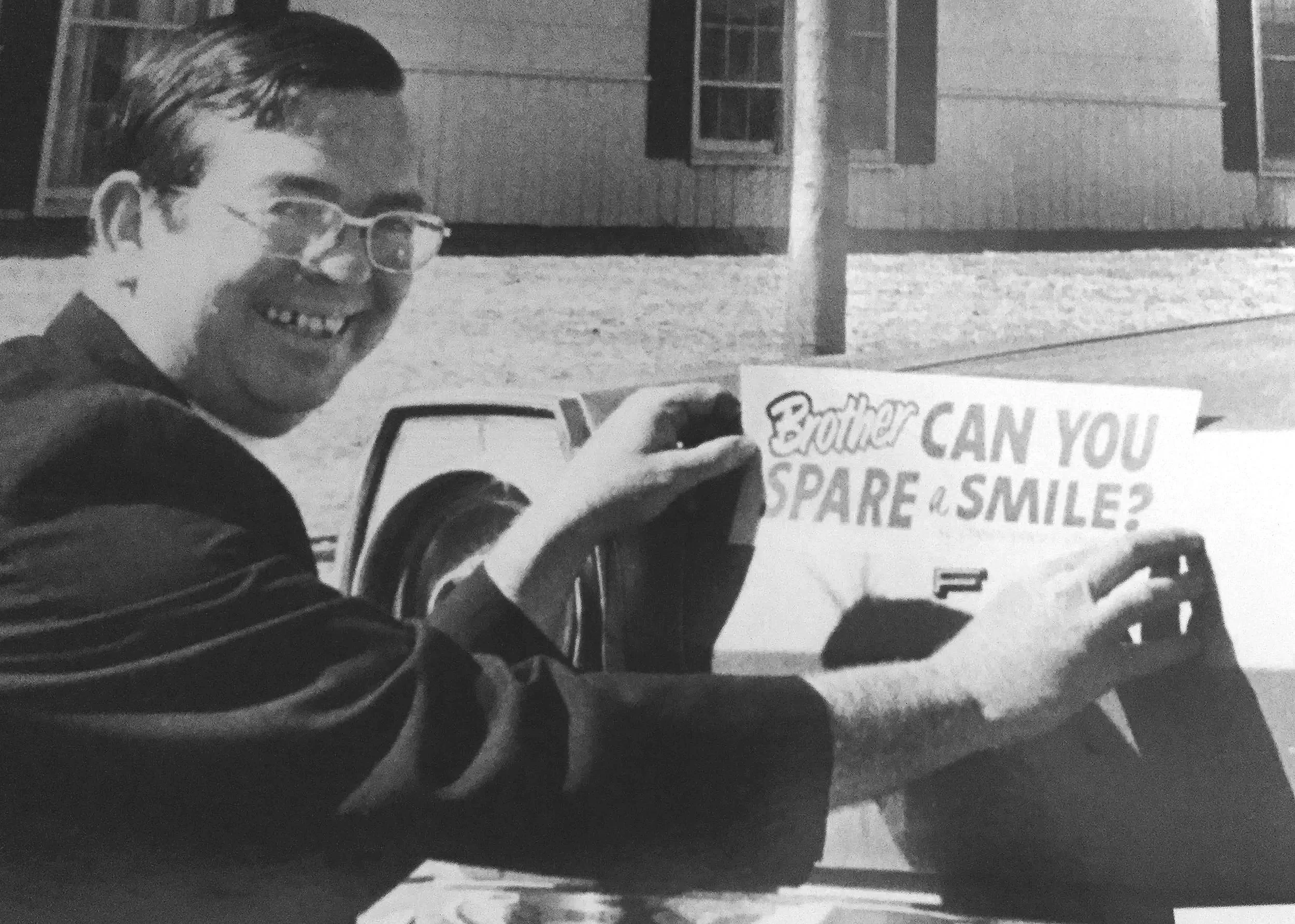 The Rev. Kenneth Clark, rector of St. Christopher's from 1969–1976. He holds up a sign reading, "Brother CAN YOU SPARE a SMILE?"