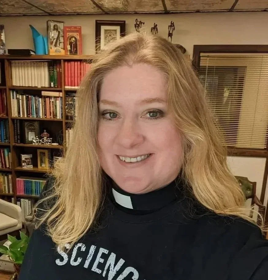 Rector Rev. Rachel Petty smiling in front of many books.