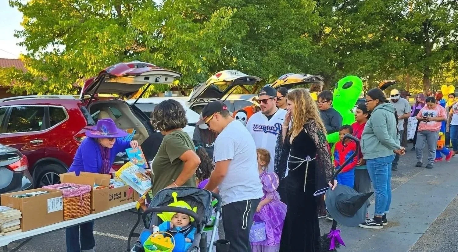 People in line at a trunk-or-treat event with cars and Halloween decorations in a parking lot.