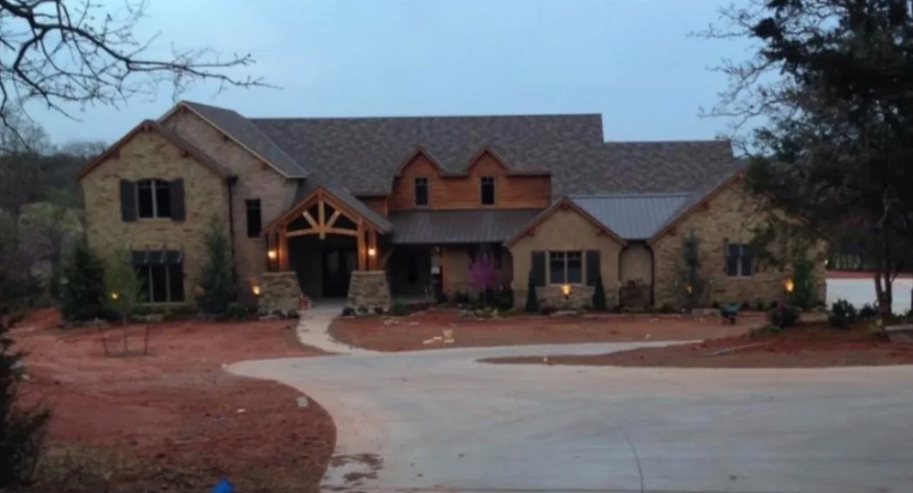 A two-story house with a stone and wood exterior, multiple windows, and a curved driveway in front.