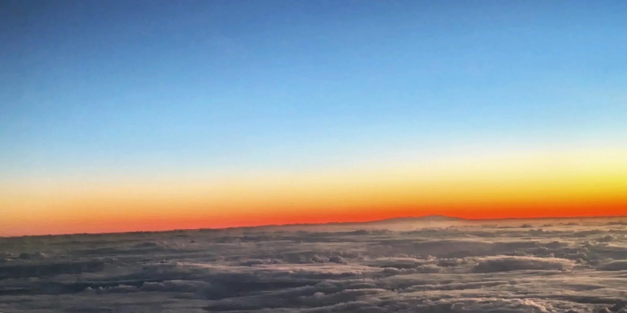 A sunset over a snow-covered mountainous landscape with a clear blue sky.