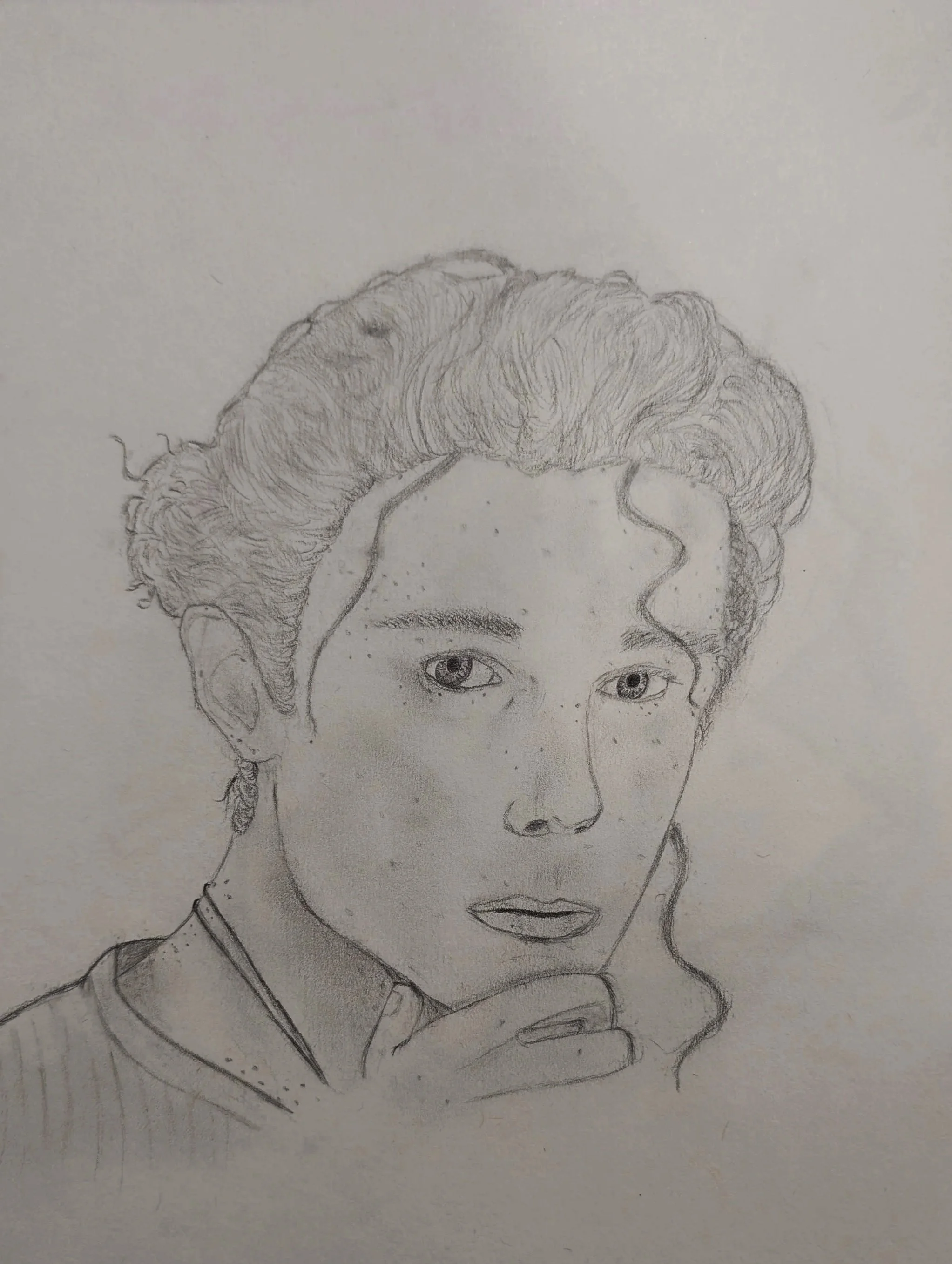 A detailed pencil sketch portrait of a woman with curly hair, freckles, and expressive eyes, resting her chin on her hand.