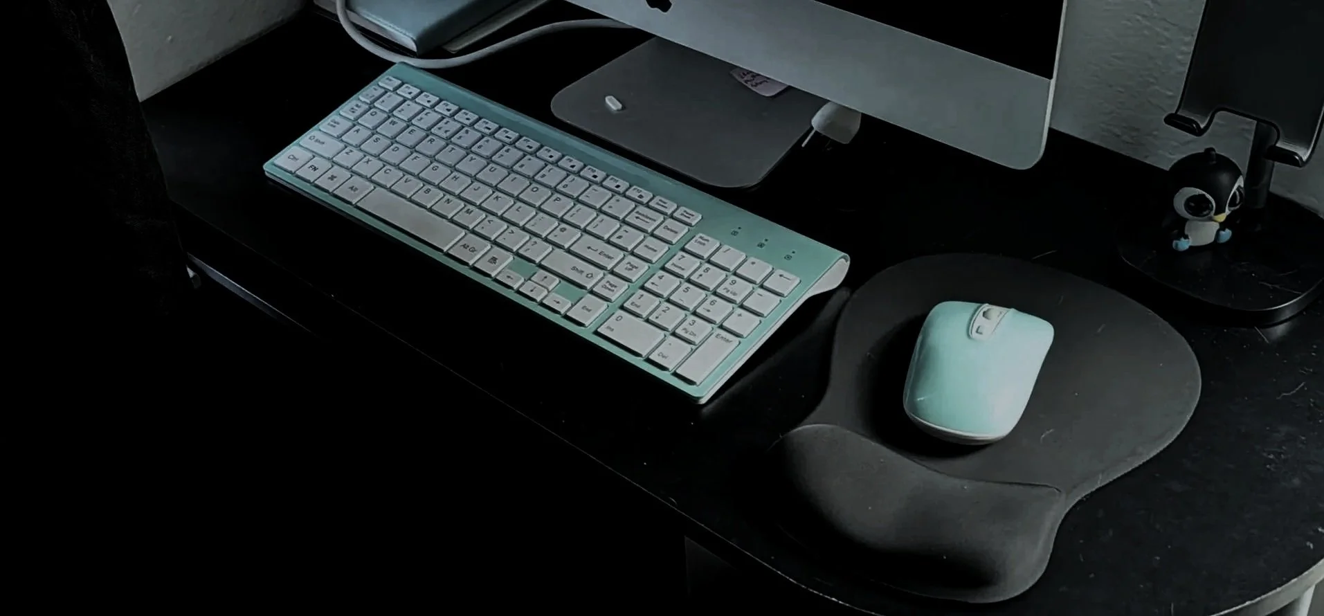 A keyboard, mouse on black desk with a computer monitor at the top