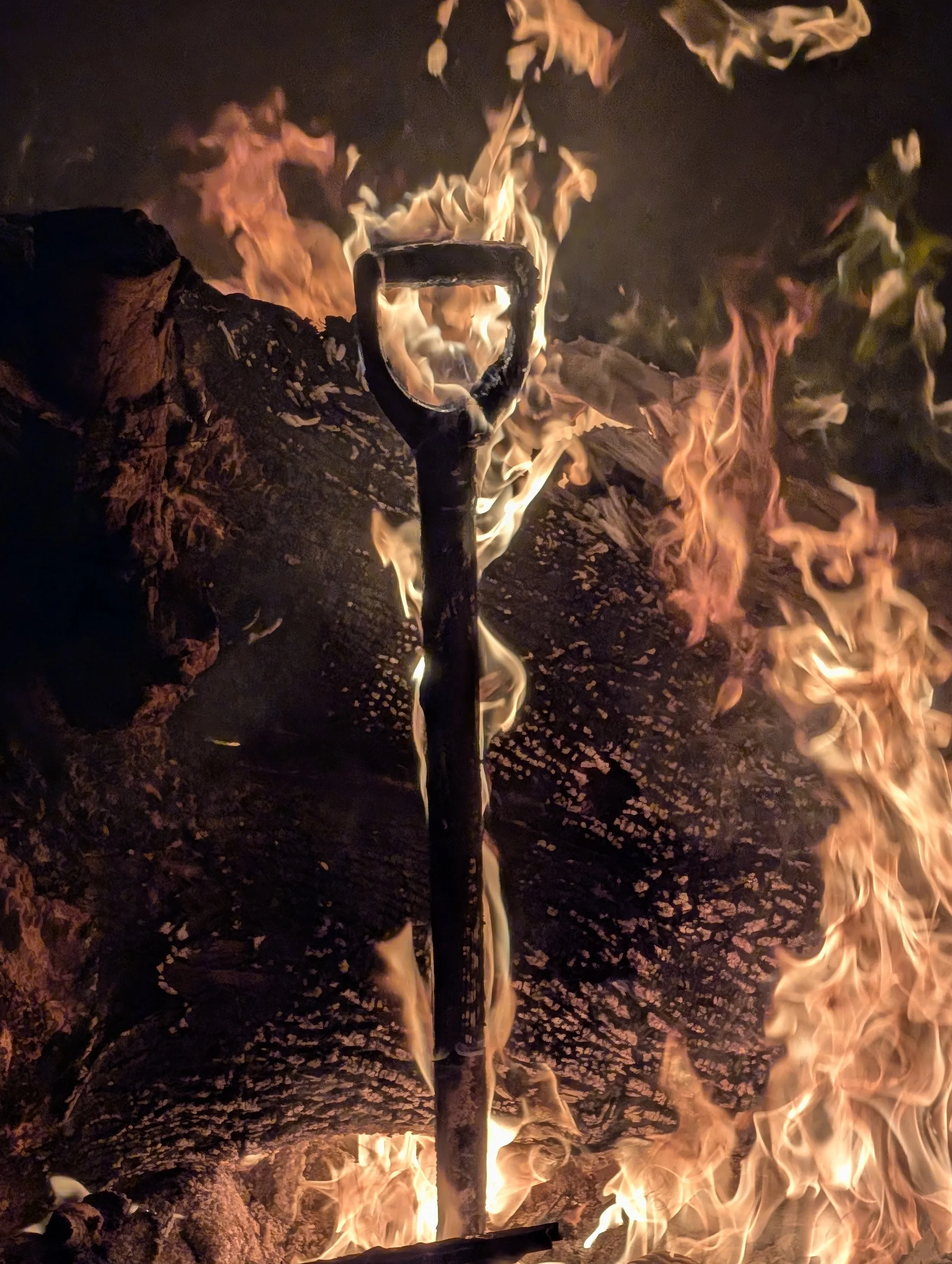 A paddle stuck in a large fire with burning logs around it.