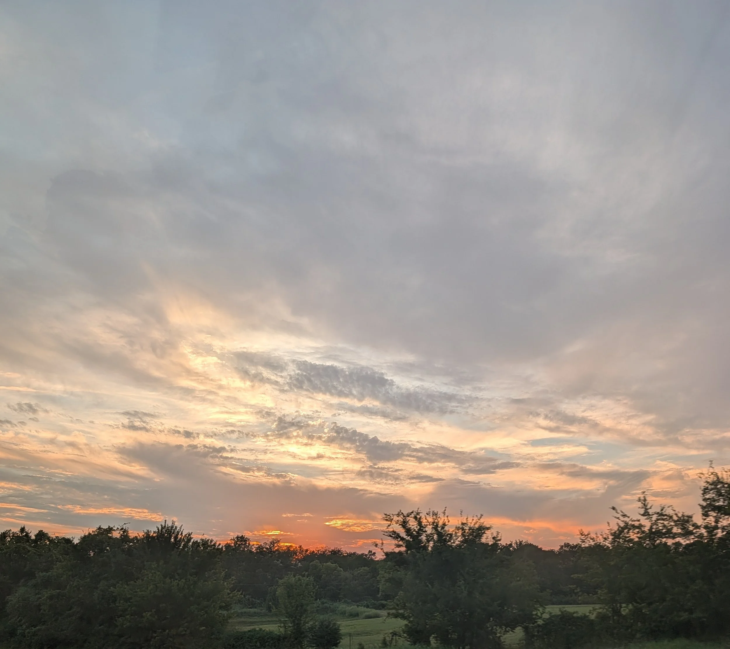 A sunset over a landscape with trees and a partly cloudy sky.