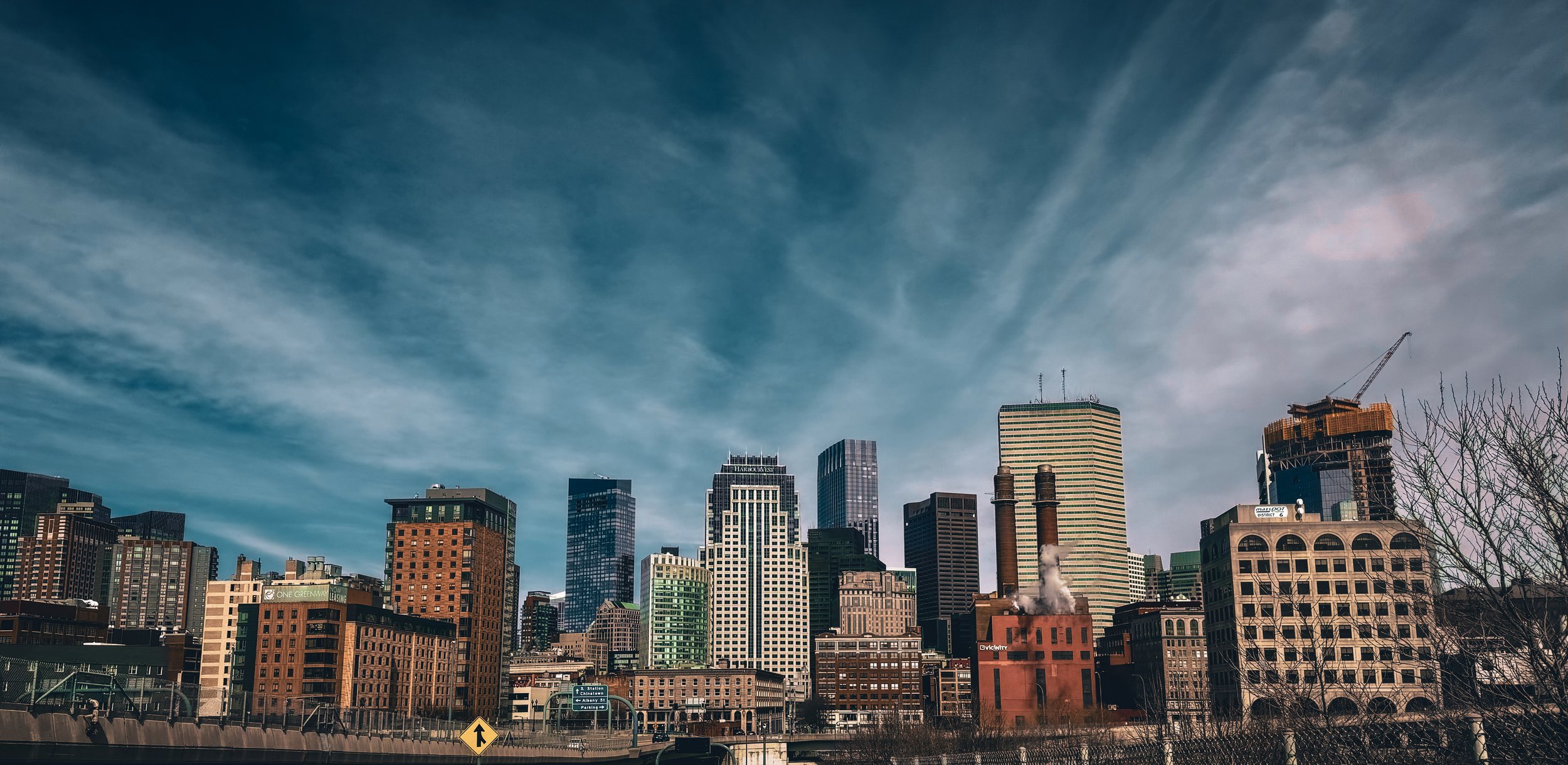 City skyline with tall skyscrapers and a partly cloudy sky.