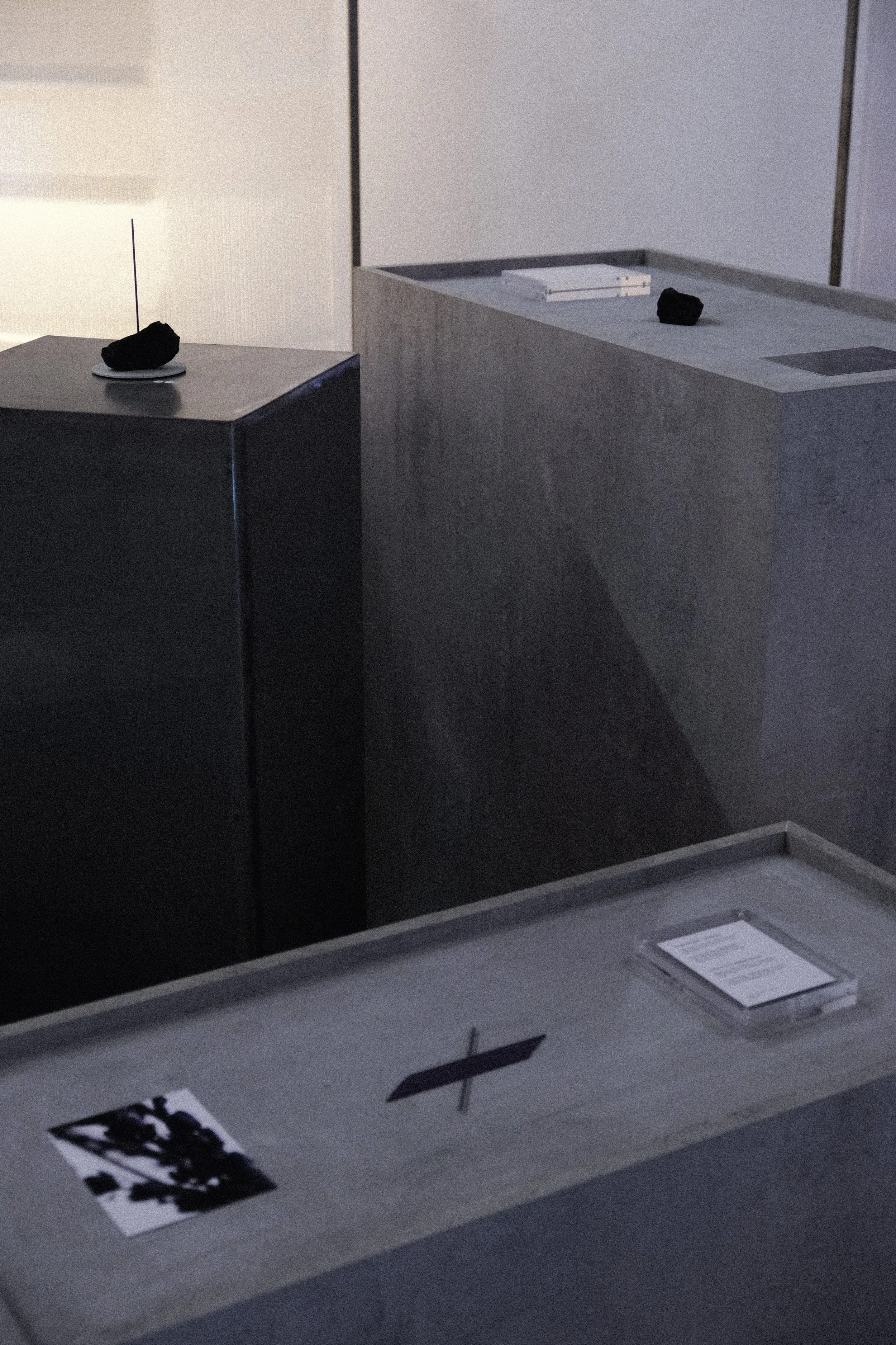Two large display cases with black rocks on white plates inside a room with papers and a pen on a desk.