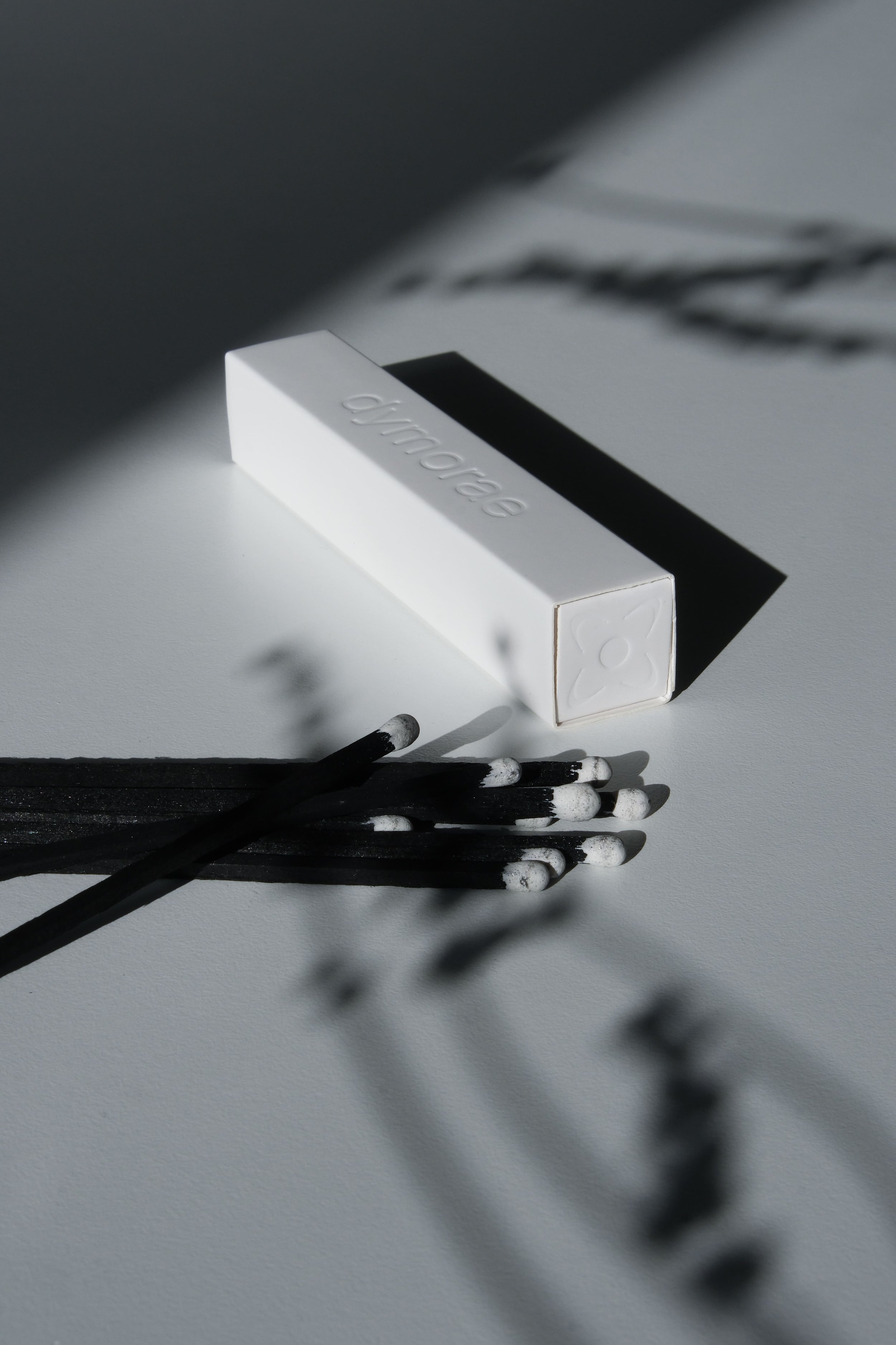 A white matchbox labeled 'dynamo' lies on a white surface, with several blackened matchsticks next to it. Shadows of the matches are cast on the surface.