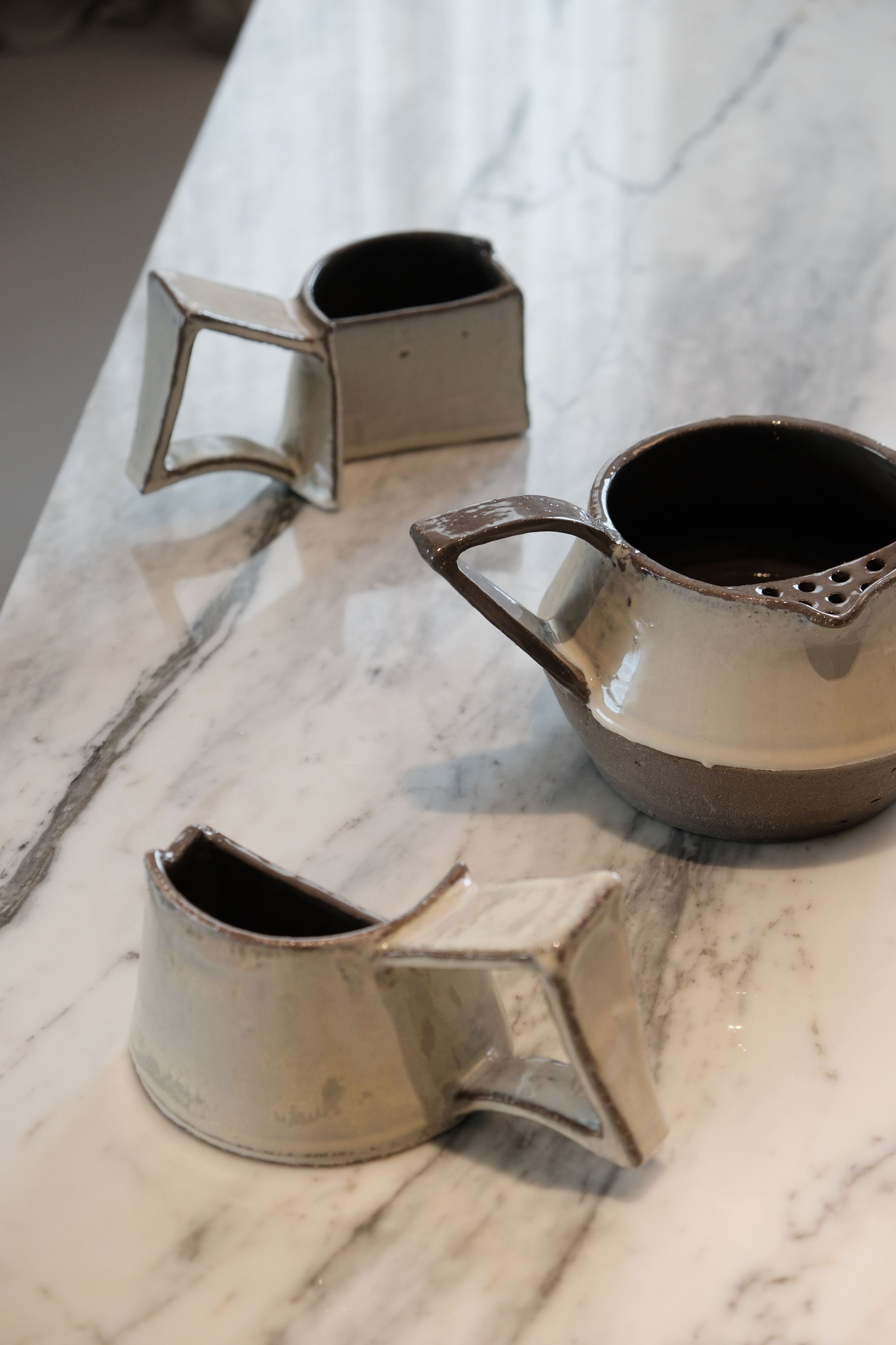 Close-up of multiple small ceramic creamers with dark interiors on a marble surface.