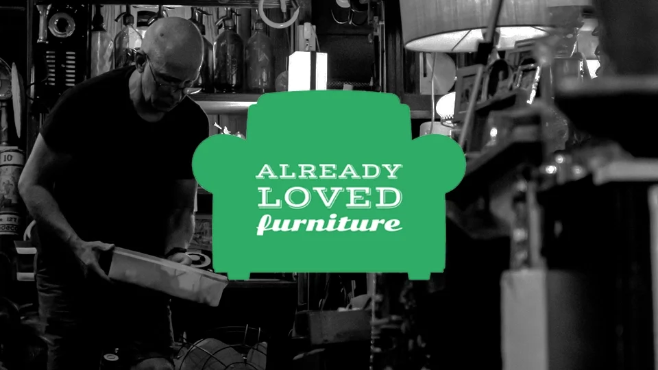 Vintage-inspired green armchair silhouette logo with serif and script typography for Already Loved Furniture, displayed over a black and white workshop photo.