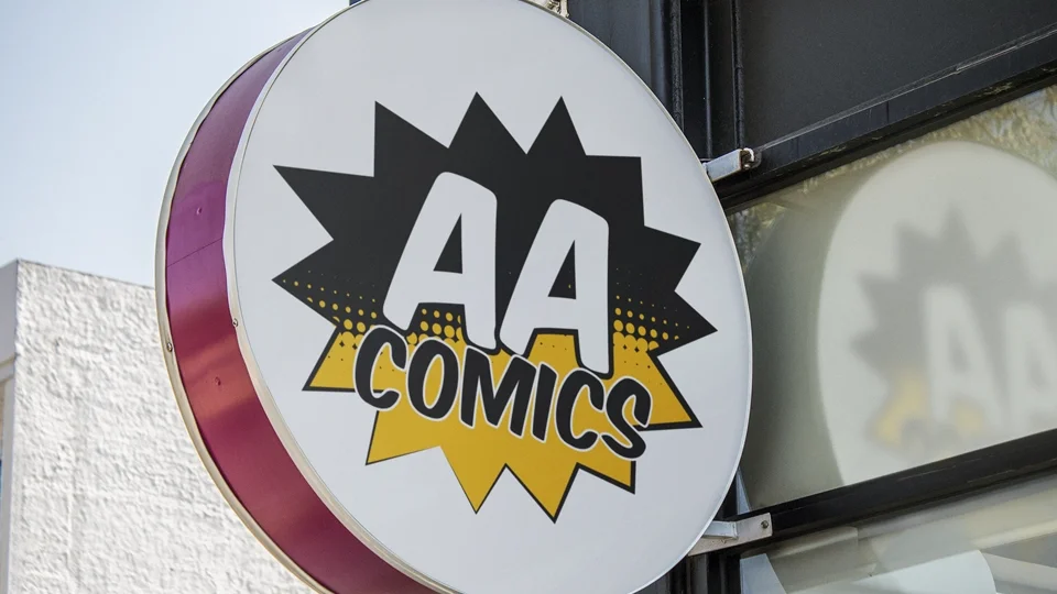 Vibrant comic book style logo for AA Comics in Wolverhampton UK with a black and yellow starburst background and bold "AA COMICS" typography on a circular outdoor storefront sign.