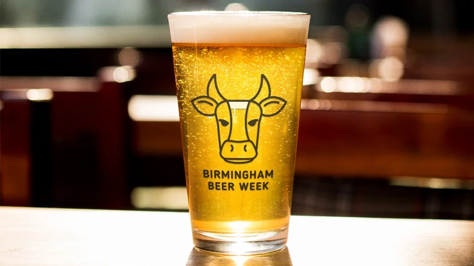 Minimalist line-art logo of a bull head with a beer glass integrated into the forehead, printed on a pint of lager for Birmingham Beer Week branding.