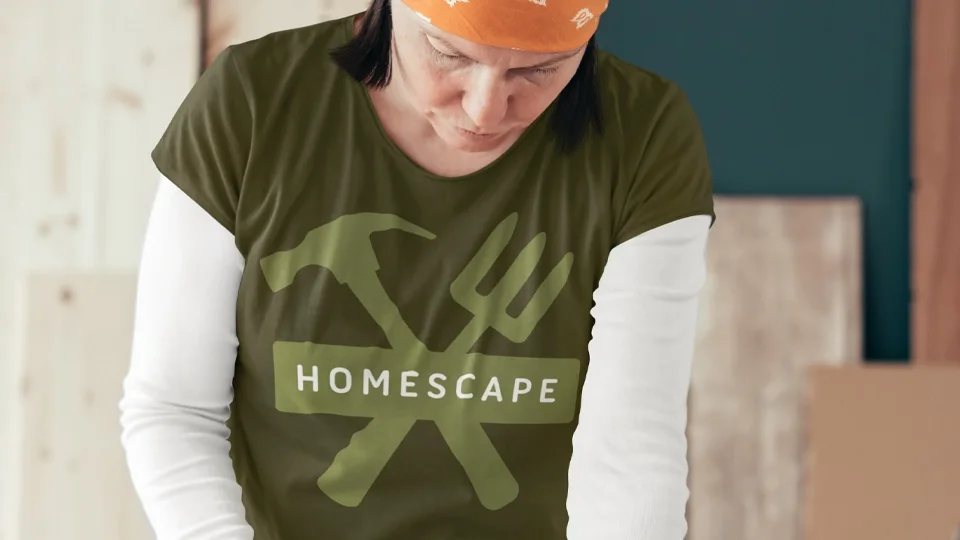 Earth-toned branding for Homescape featuring a crossed hammer and garden fork icon with clean sans-serif typography on an olive green work t-shirt.