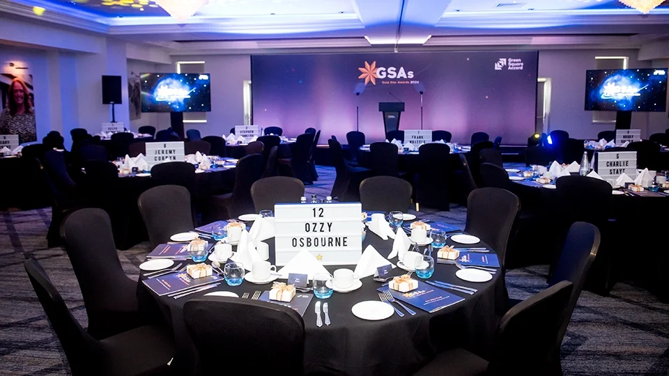 A wide-angle view of a professionally designed event space. The design features cohesive branding from the large-scale stage backdrop to the individual table markers and printed menus, all utilizing a deep blue and gold celestial color palette.