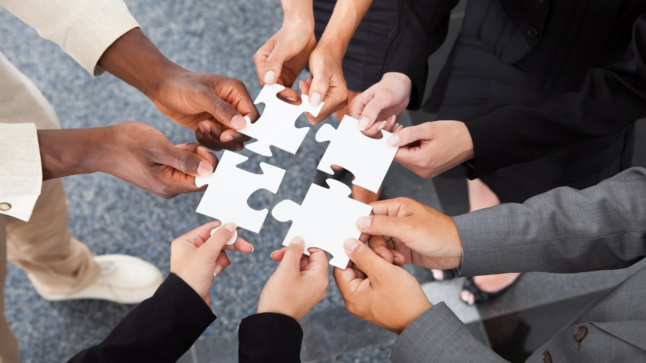 Five people holding interconnected white puzzle pieces in a circle, symbolizing teamwork and collaboration.