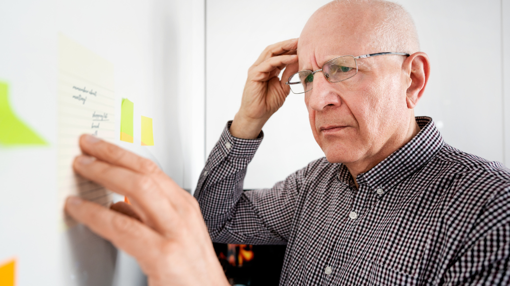 A middle-aged man with glasses and a checkered shirt looks focused as he places sticky notes on a white wall.