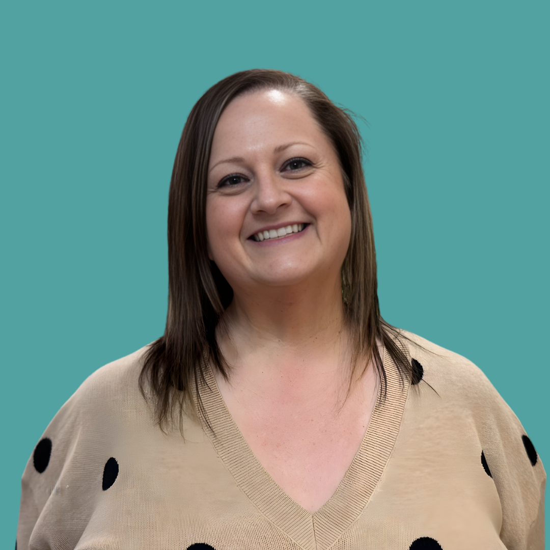 A woman with shoulder-length brown hair smiling against a teal background, wearing a beige sweater with black polka dots.