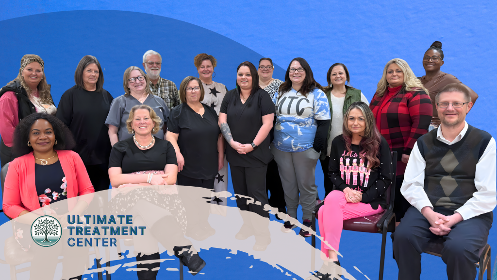 Group of 15 diverse individuals posing together in front of a blue backdrop, with the Ultimate Treatment Center logo in the foreground.