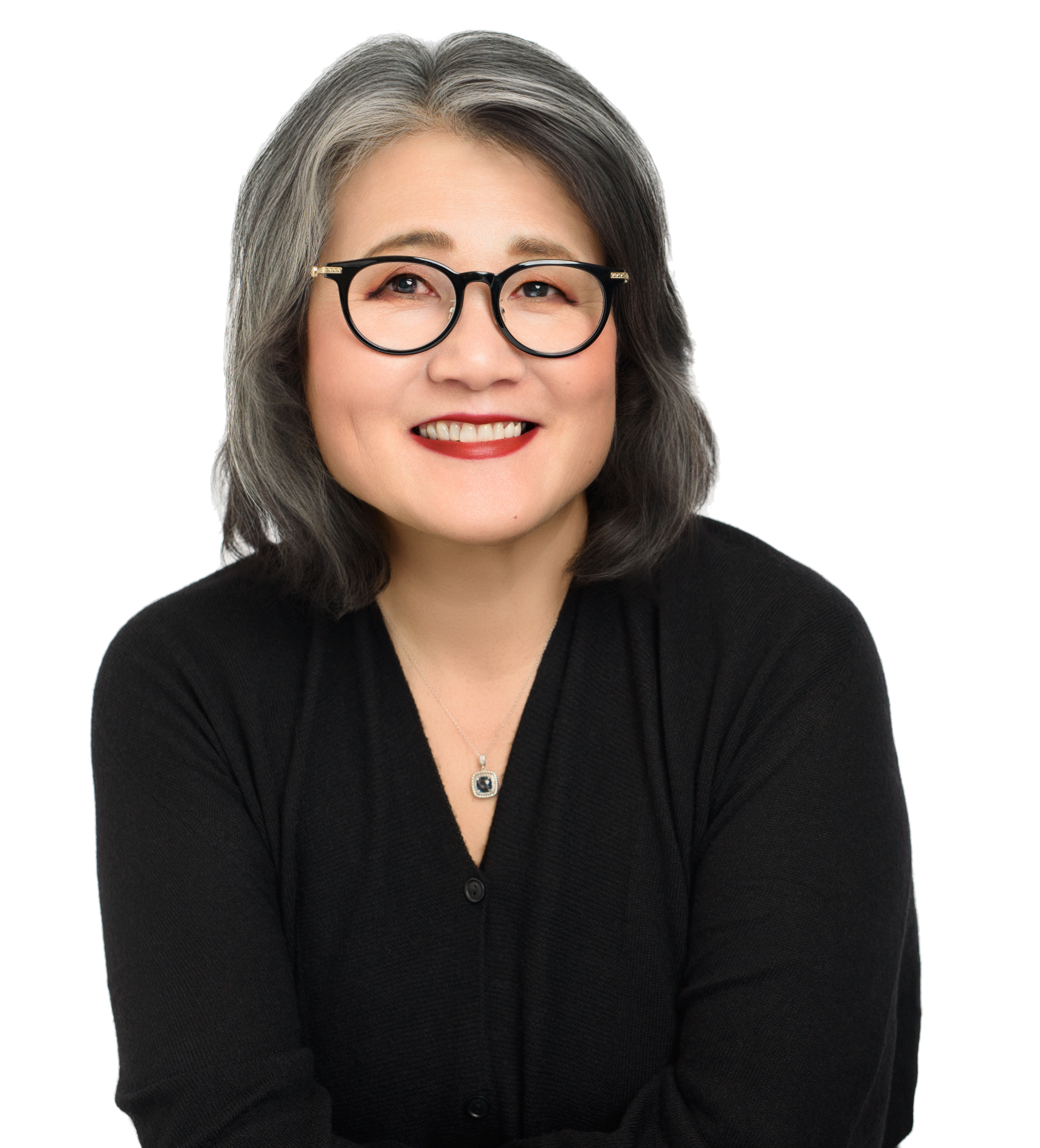 A smiling woman with shoulder-length gray hair wearing black glasses and a black top, with a background that is partially white and partially black and gray.