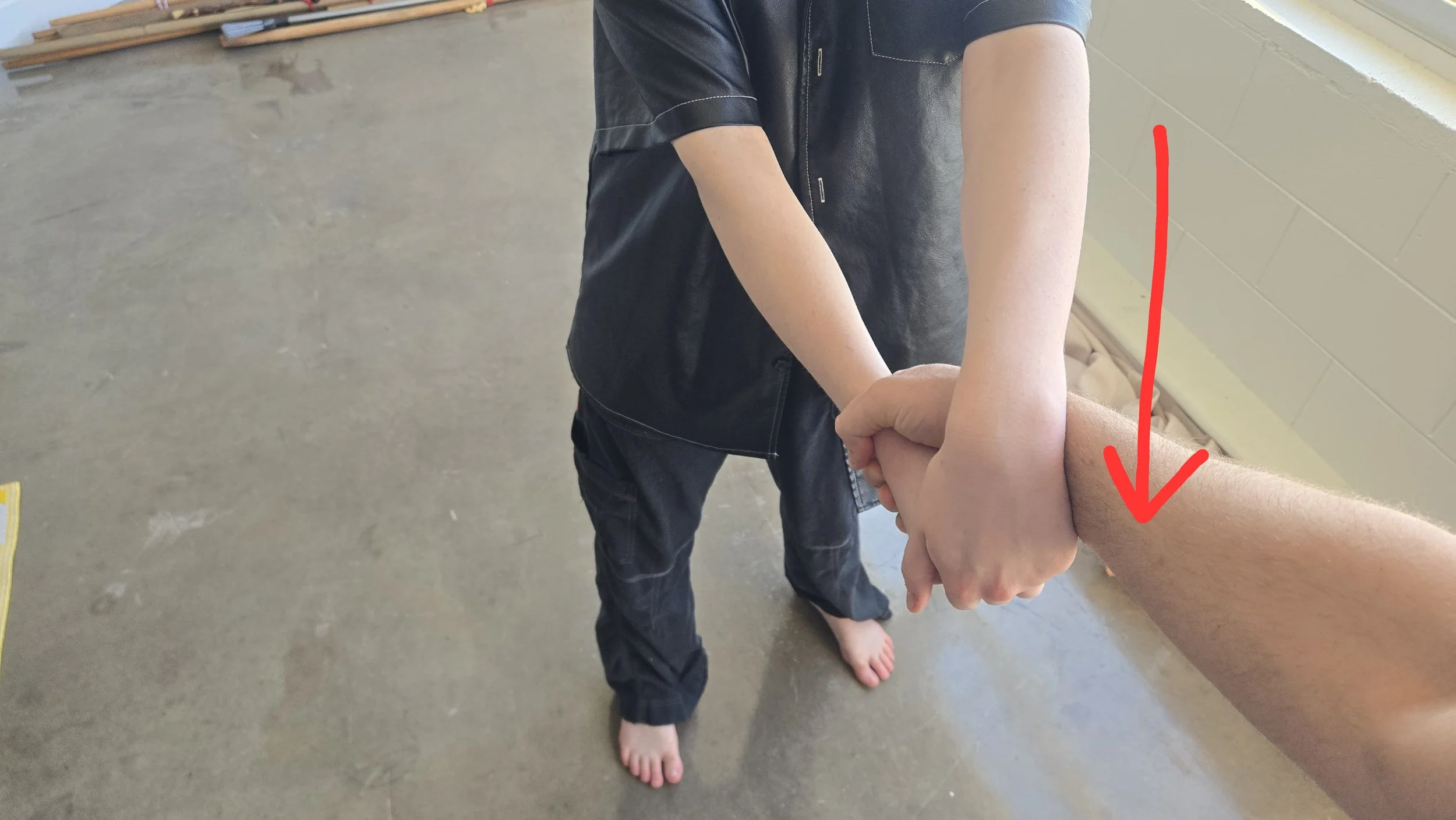 Me reaching over the man's arm to grab my fist. There is an arrow pointing out how I go directly over the attacker's arm,
