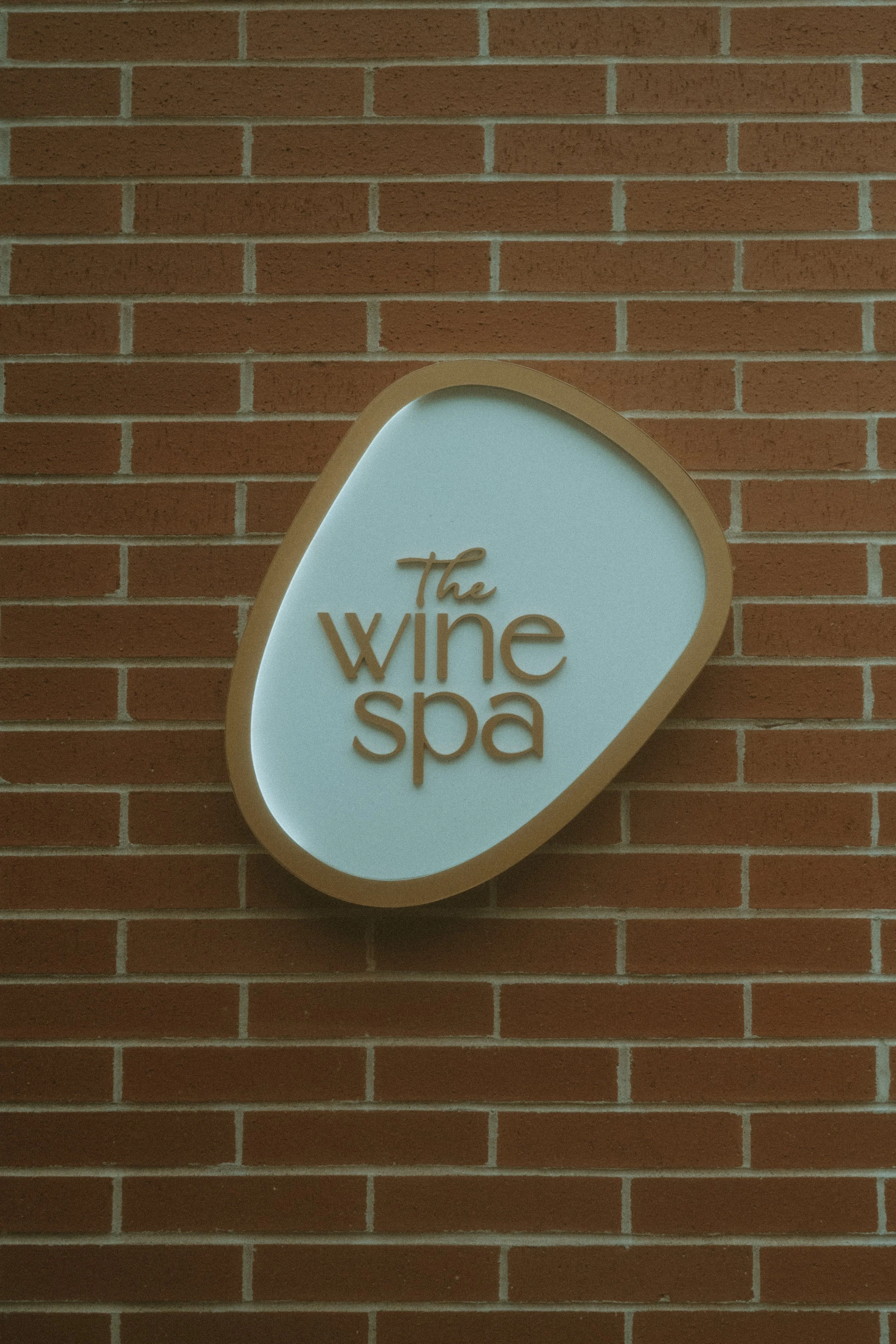 Sign for the Wine Spa mounted on a brick wall, with a rounded shape, light background, and brown lettering.