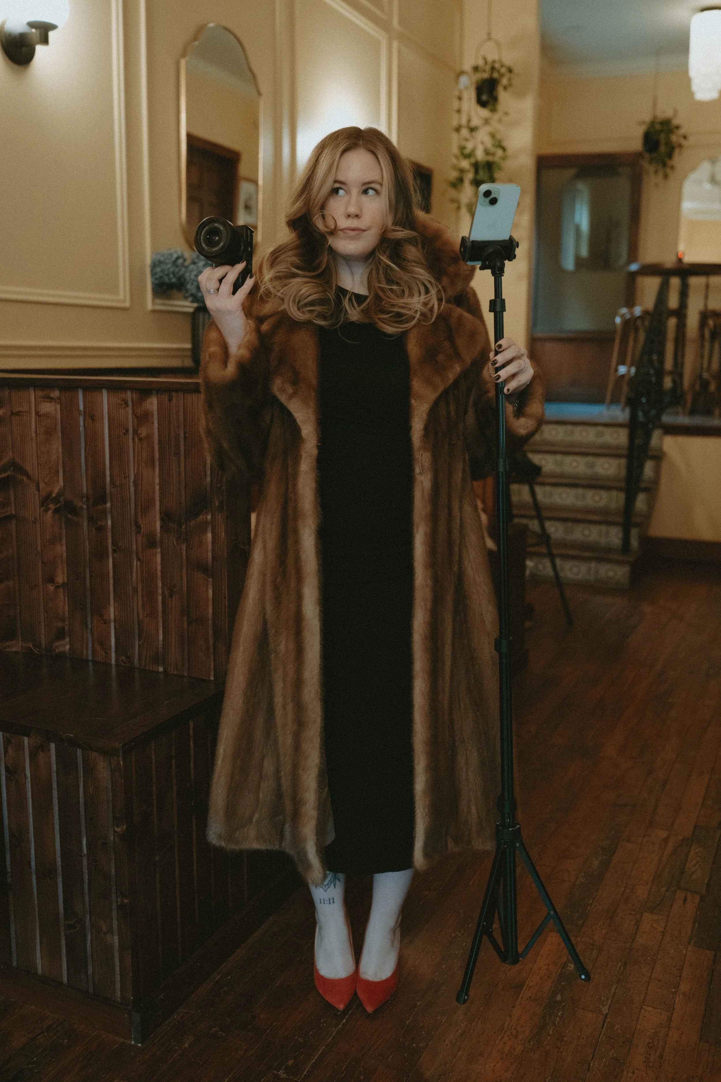 A woman is taking a photo with a camera on a tripod inside a room with large windows and a Christmas tree in the background.