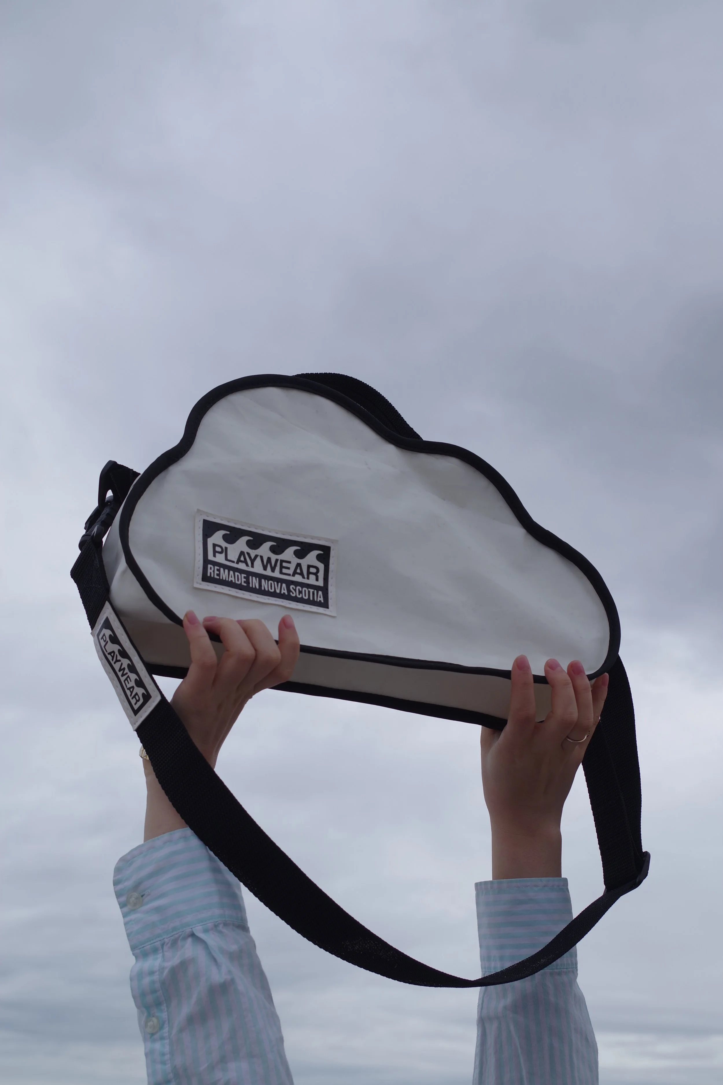 Person holding a white surfboard bag with a black strap, against a cloudy sky.