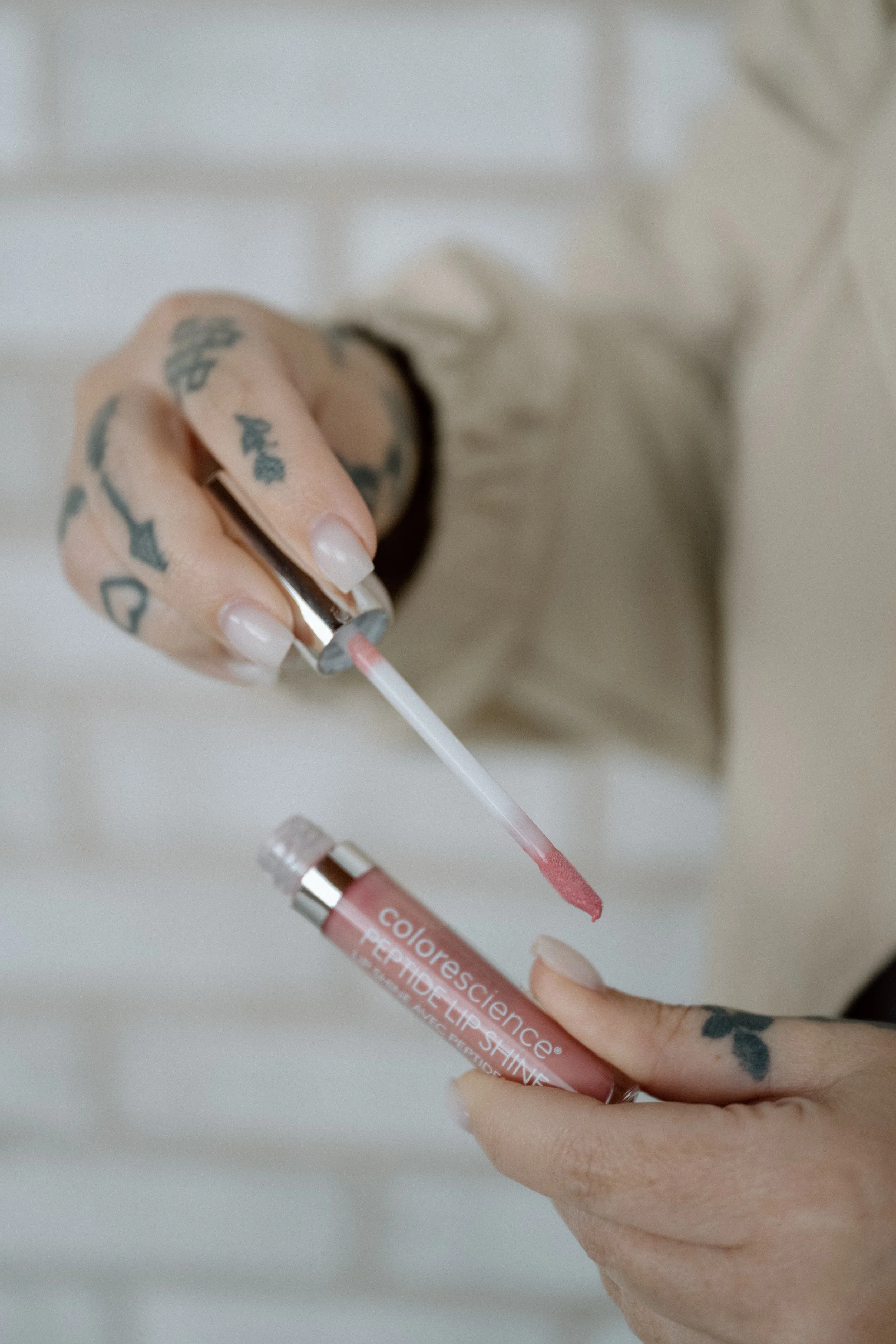 Two hands holding a light pink lip gloss, open with applicator shown