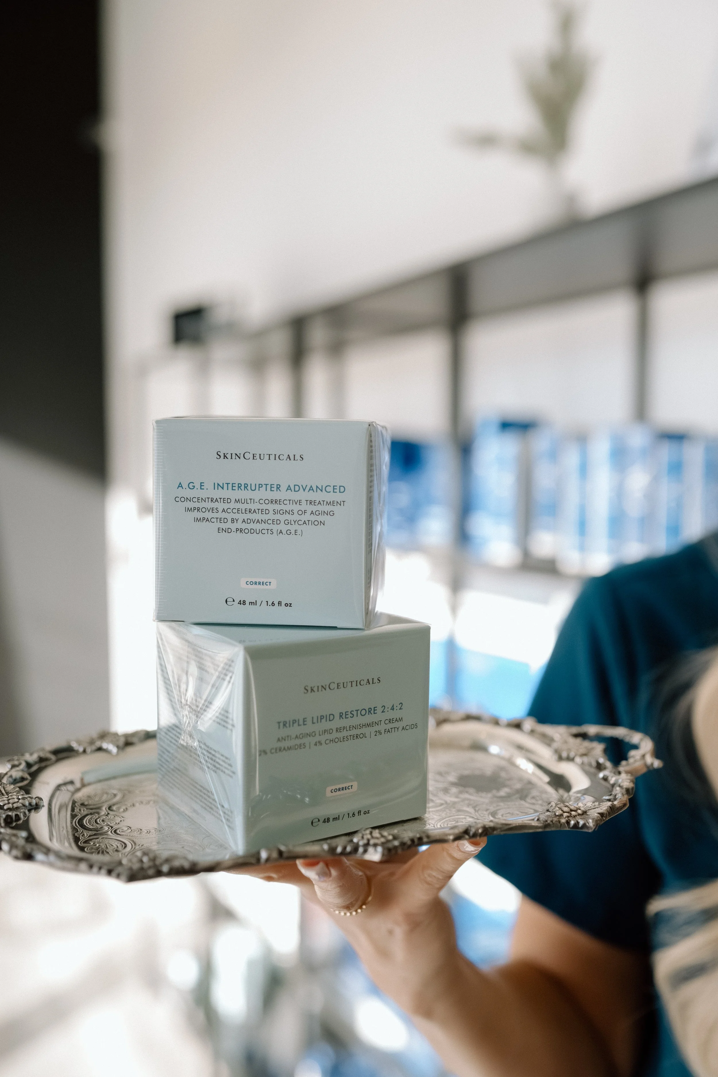 A hand holding up a silver tray, with two product boxes sitting on the silver tray, in aqua blue boxes