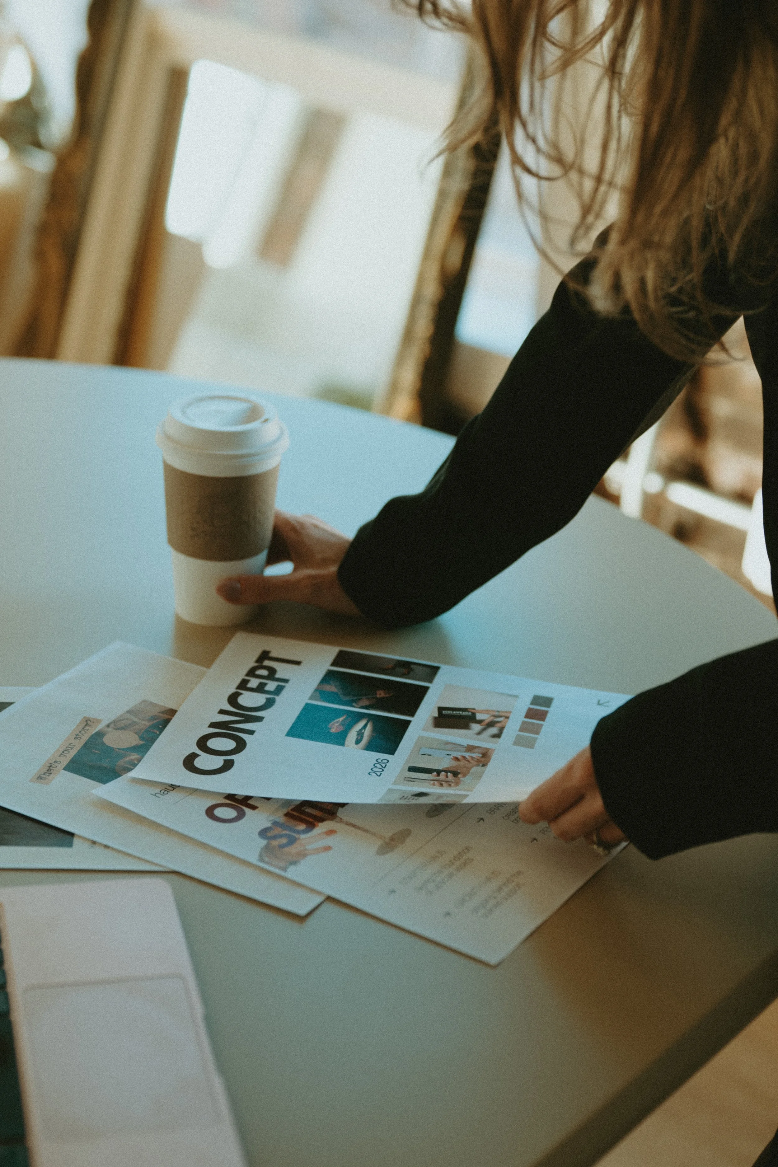 Person reaching for a coffee cup on a table with a concept magazine and documents.