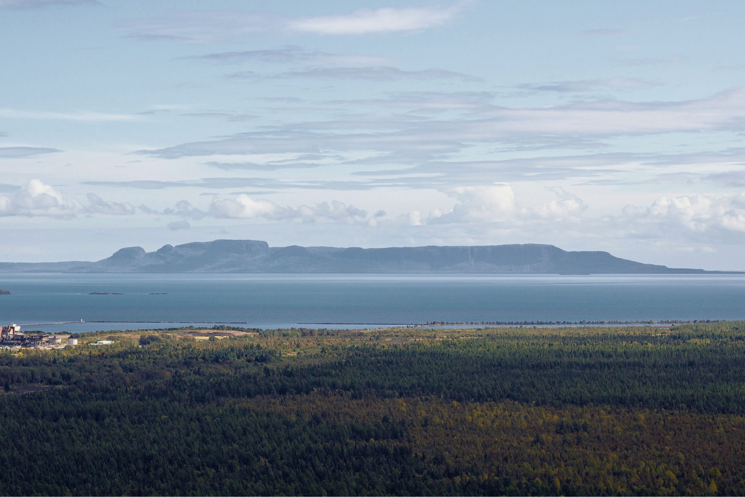 A scenic view of a large body of water with a mountain range in the background, and a forested landscape in the foreground.