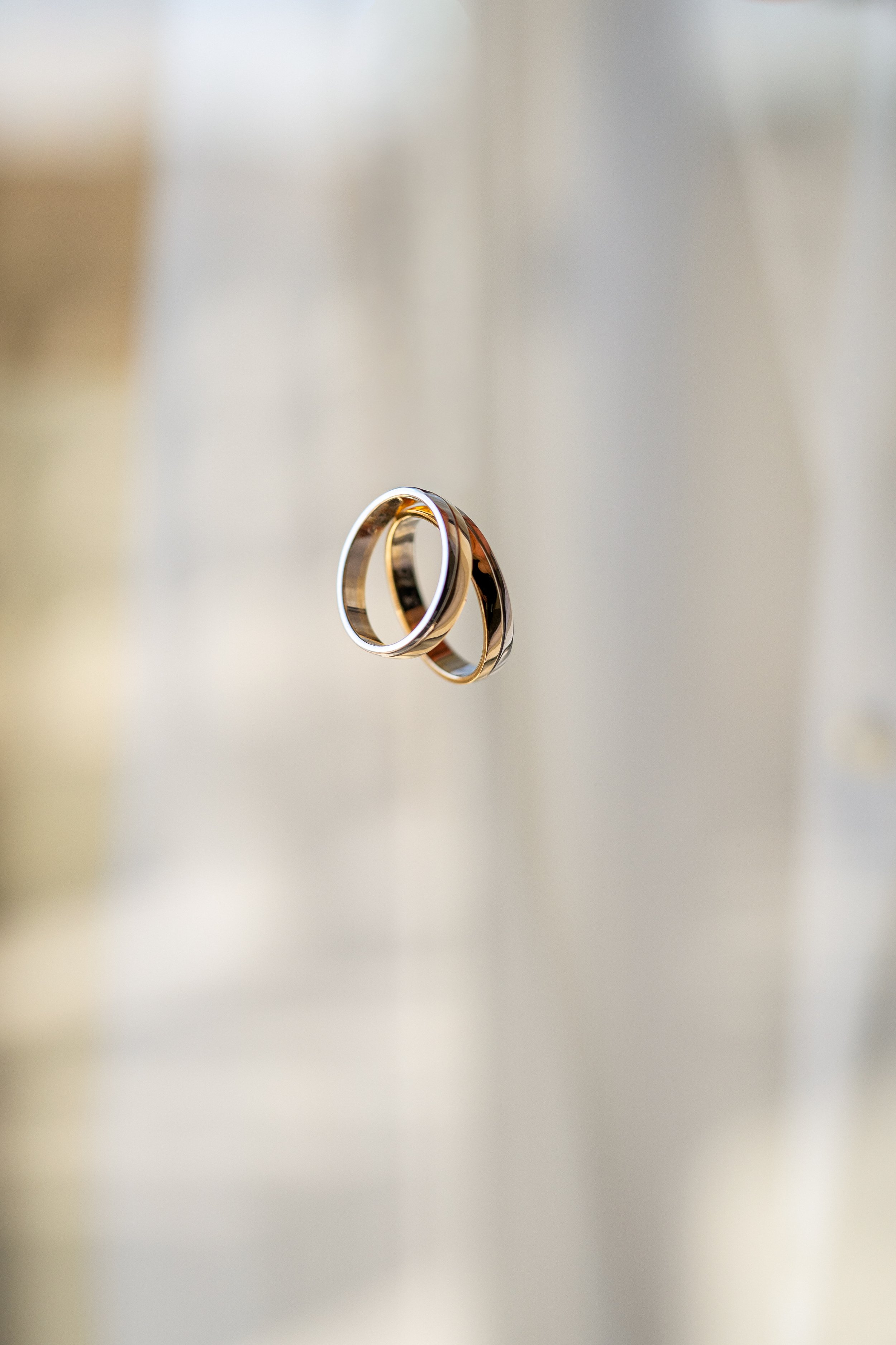 Two wedding rings, one gold and one silver, floating against a soft, blurred background.