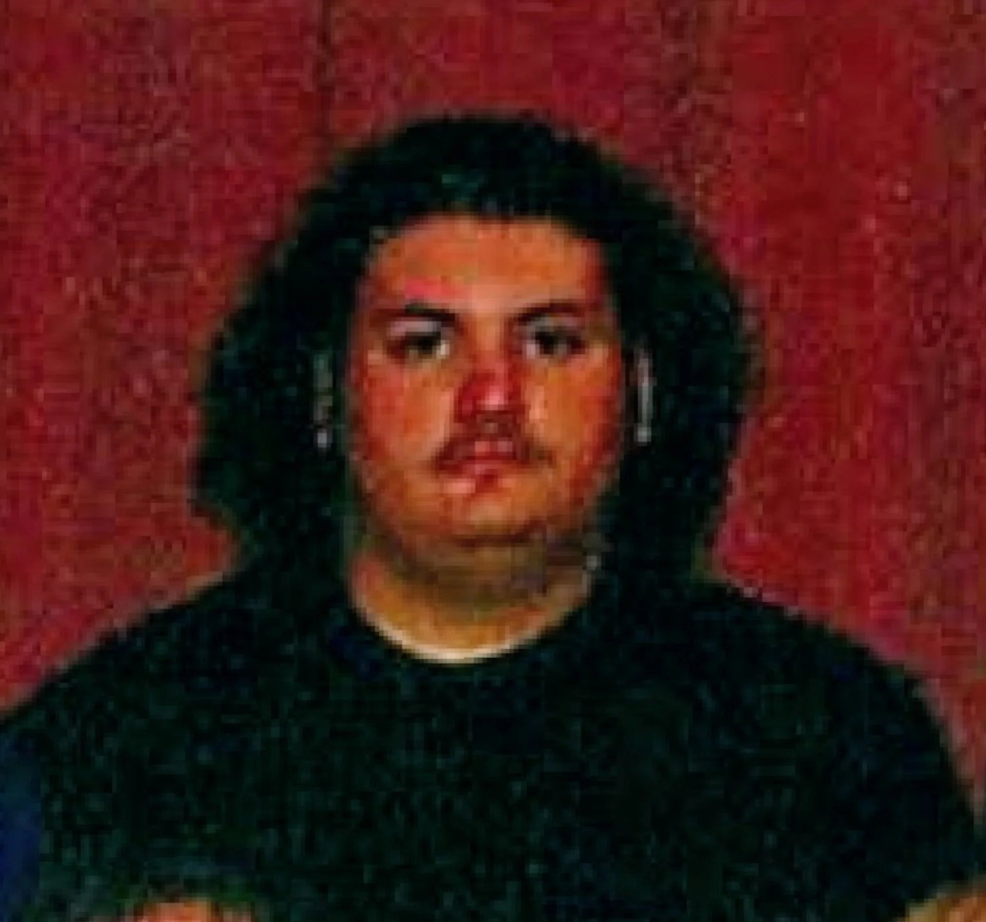 A woman with shoulder-length black hair, wearing earrings, dressed in a black top, standing against a red textured background.