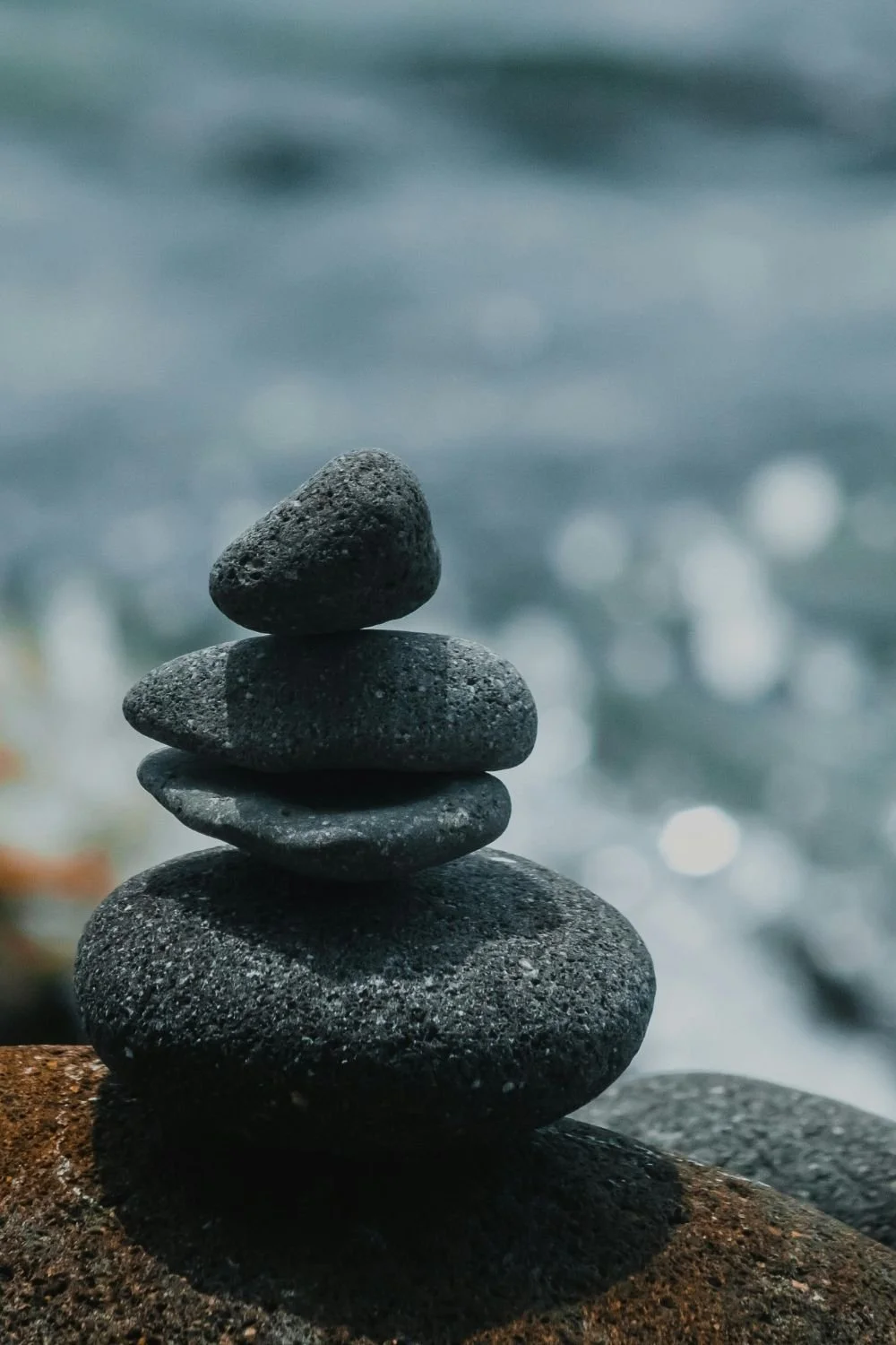 Stacked smooth black stones on a brown rock near water with blurred background.